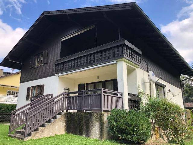 Ansicht des Hauses mit dunklem Dach, Balkon und Außentreppe in ländlicher Umgebung.