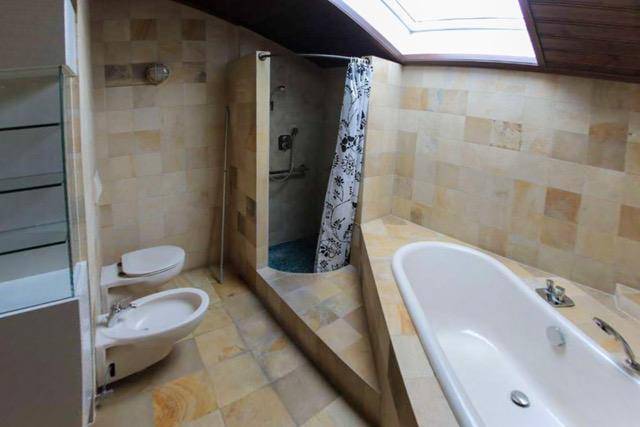 Badezimmer mit Fliesen, Badewanne, Dusche, Bidet und Dachfenster für natürliches Licht.