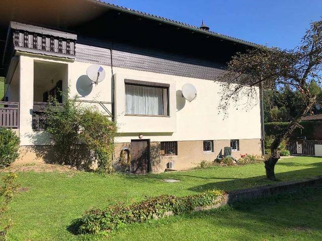 Seitenansicht des Hauses mit Rasenfläche, Bäumen und Satellitenschüsseln an der Fassade.