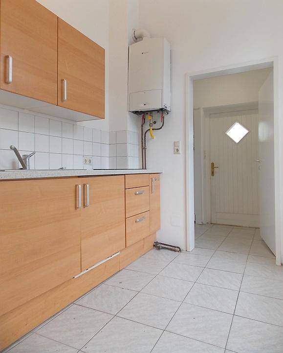 Funktionale Küche mit Holzschränken, Fliesenboden und sichtbarer Gastherme an der Wand.