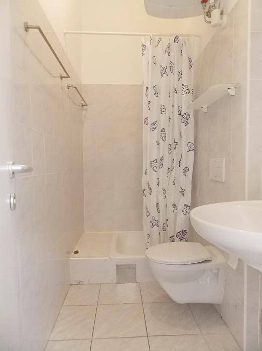 Kleines Badezimmer mit Dusche, wandhängendem WC, Waschbecken und weißen Fliesen.