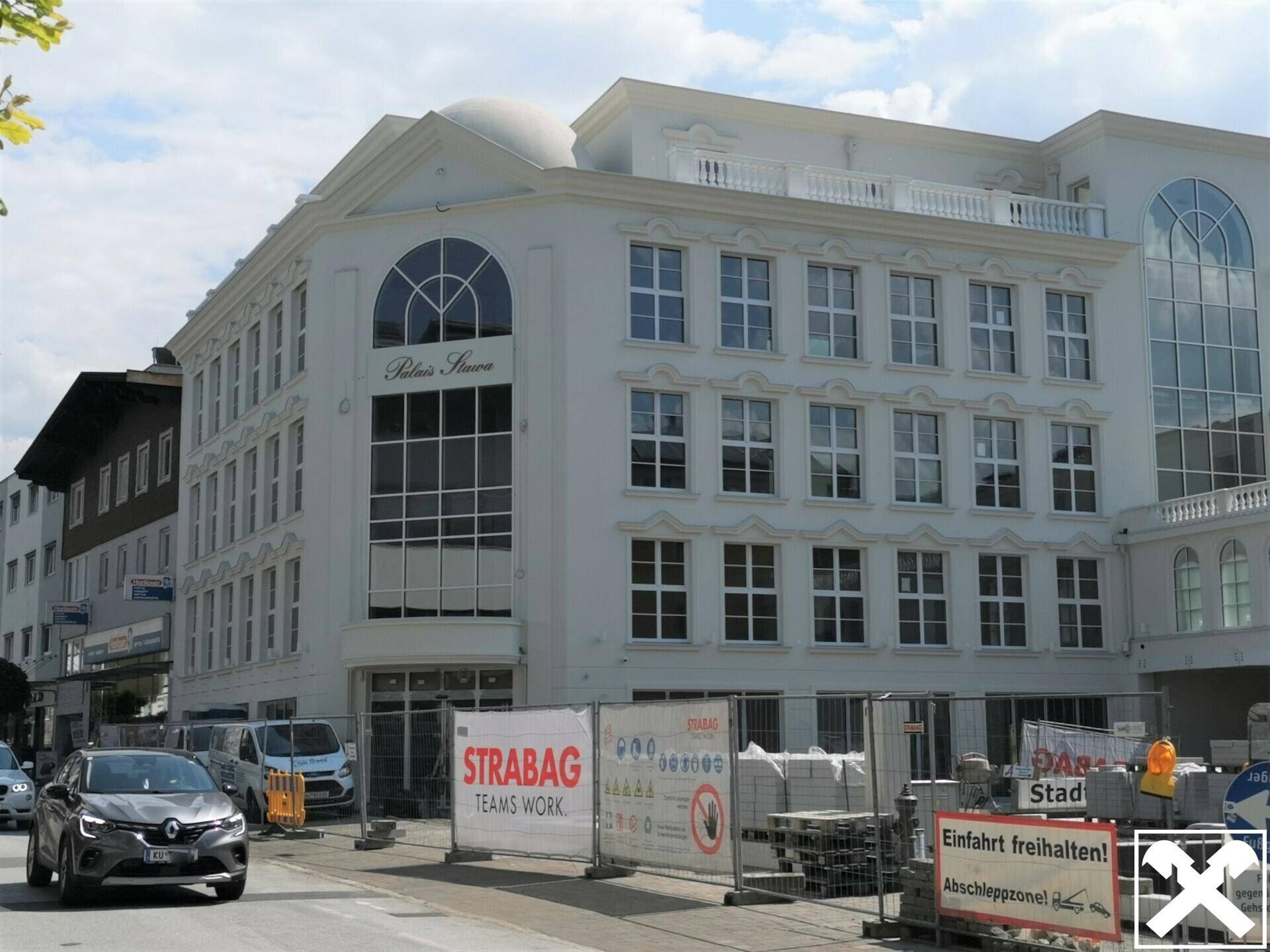 Nahaufnahme des weißen Gebäudes mit klassischer Fassade, großen Fenstern und Baustellenabsperrungen im Vordergrund.