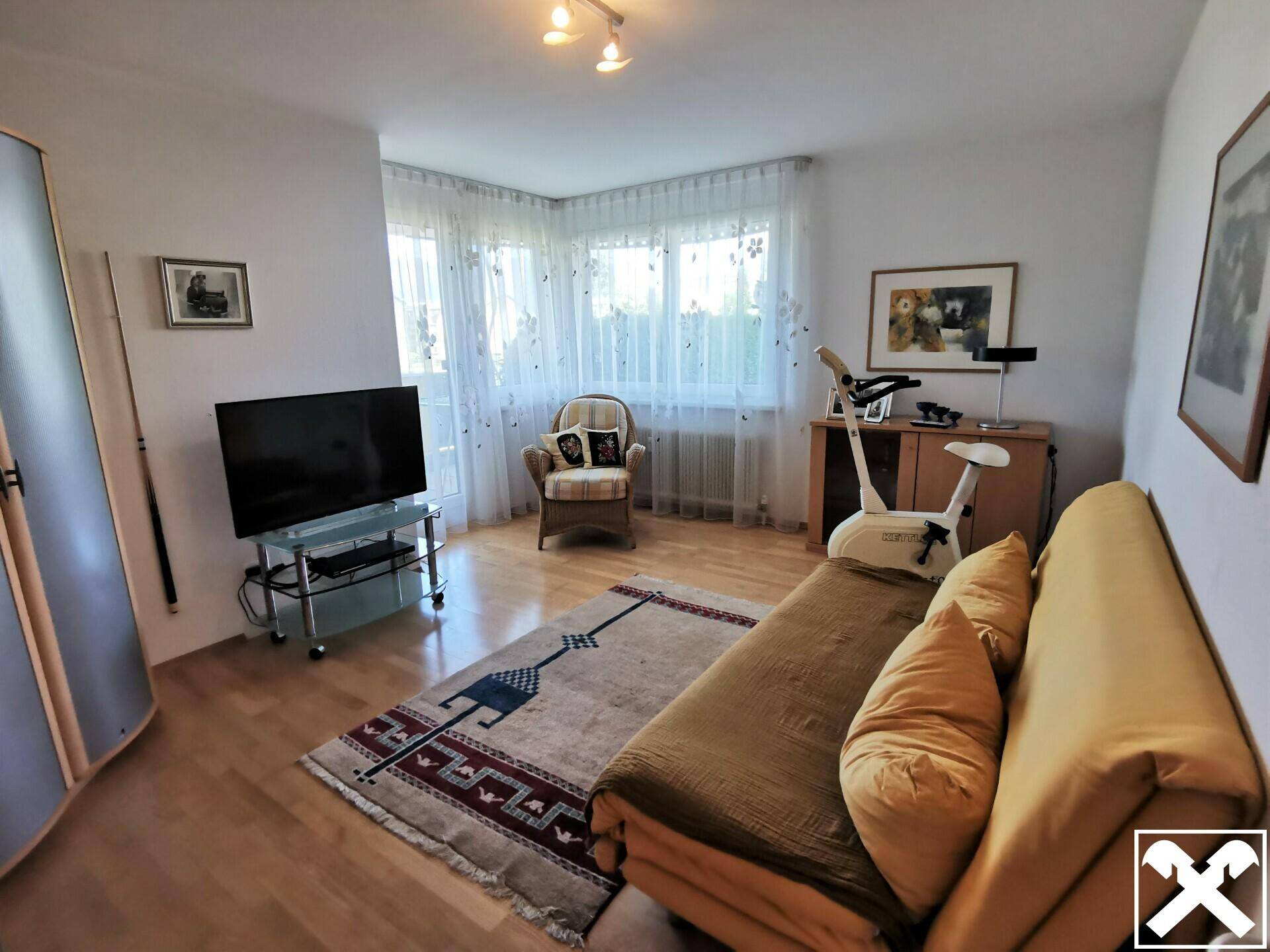 Vielseitig nutzbarer Raum mit Schlafsofa, Fernseher und Fenstern, die viel Tageslicht bieten.