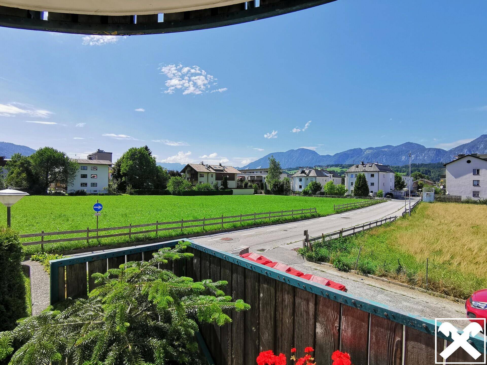 Weitläufiger Blick von der Immobilie auf grüne Felder, umliegende Häuser und die majestätischen Berge im Hintergrund.