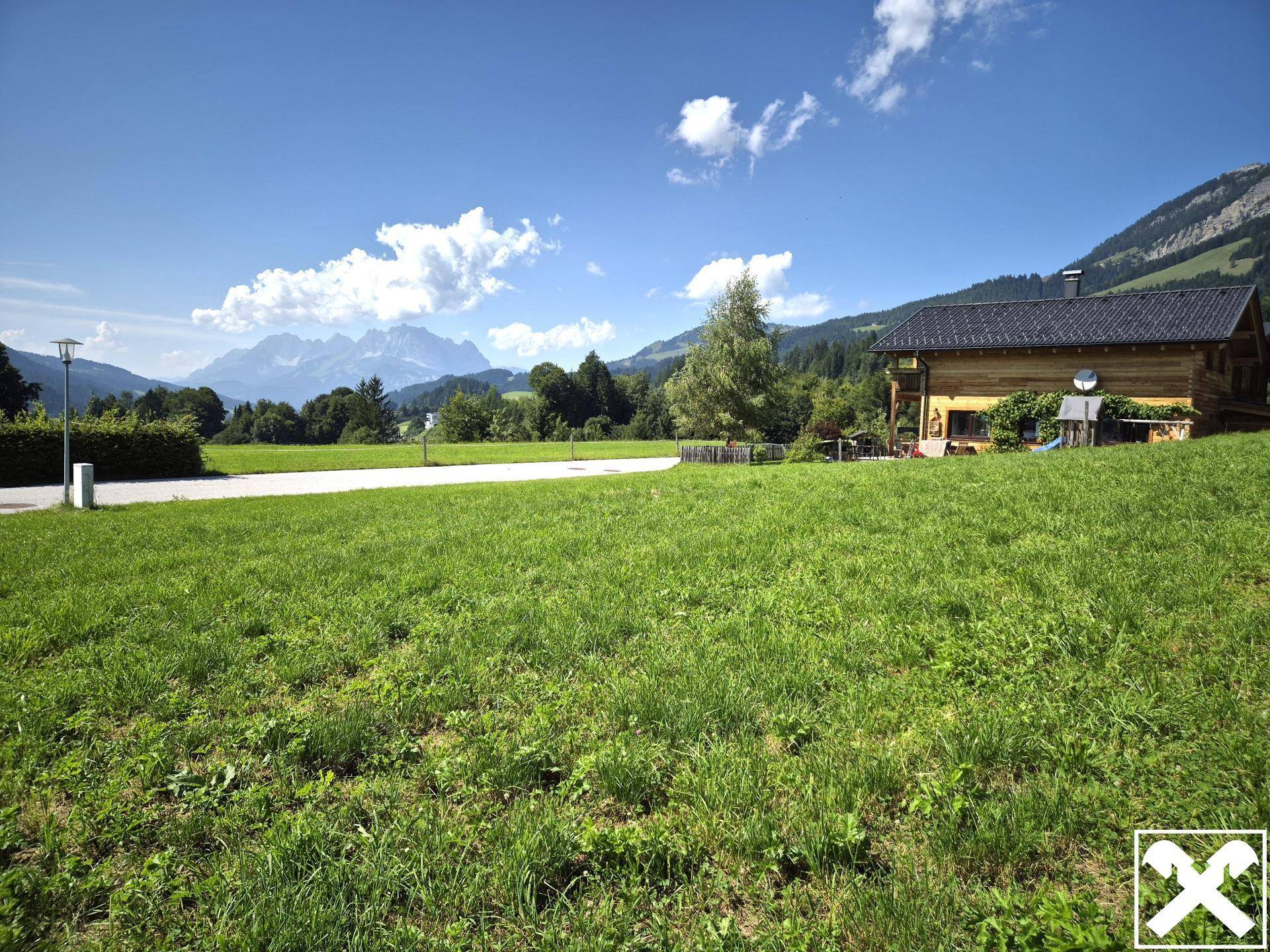 Idyllische Wiesenlandschaft mit einem traditionellen Holzhaus und beeindruckendem Alpenpanorama.