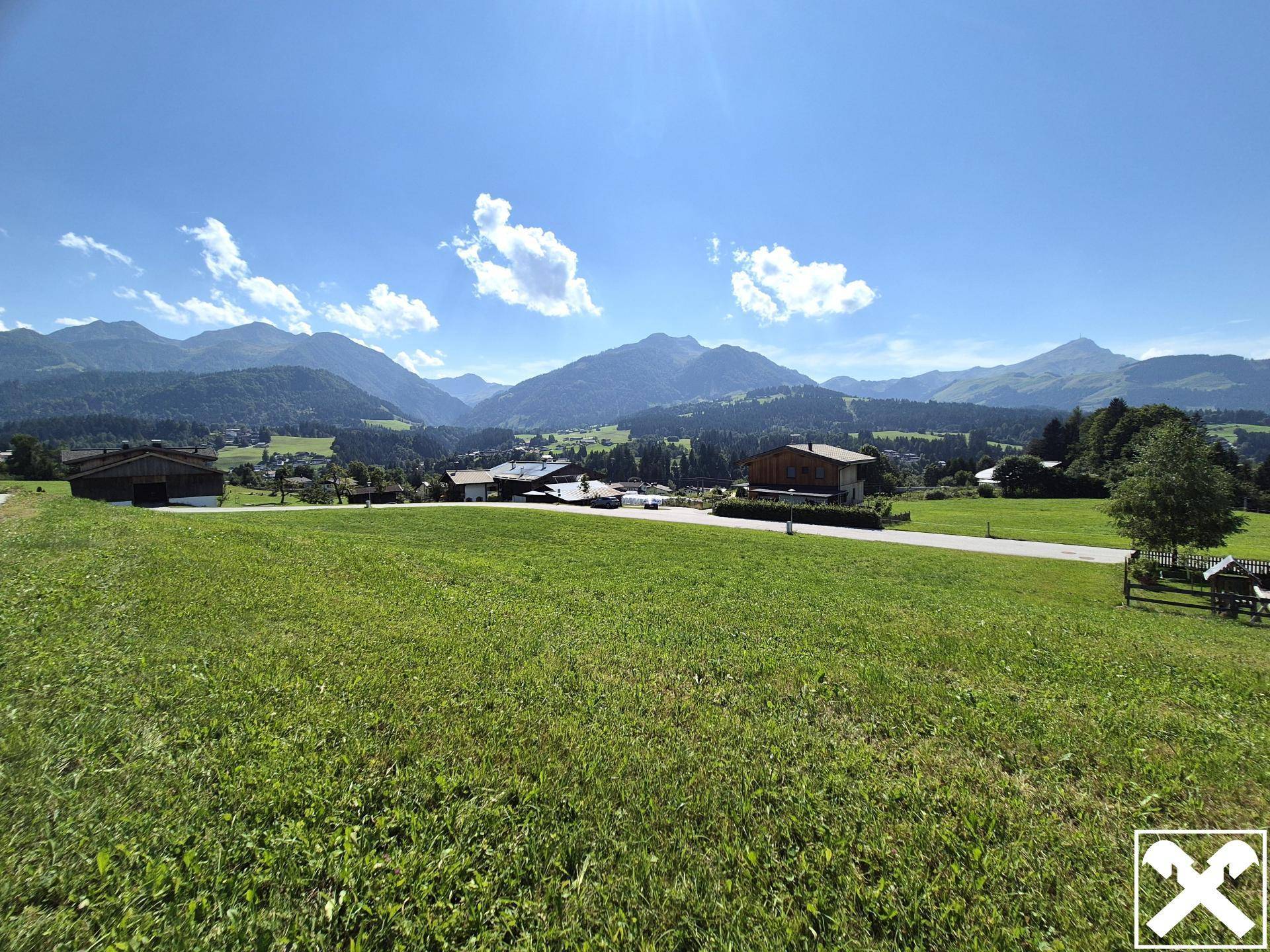 Weitläufige grüne Landschaft mit malerischem Bergblick und vereinzelten Häusern unter blauem Himmel.