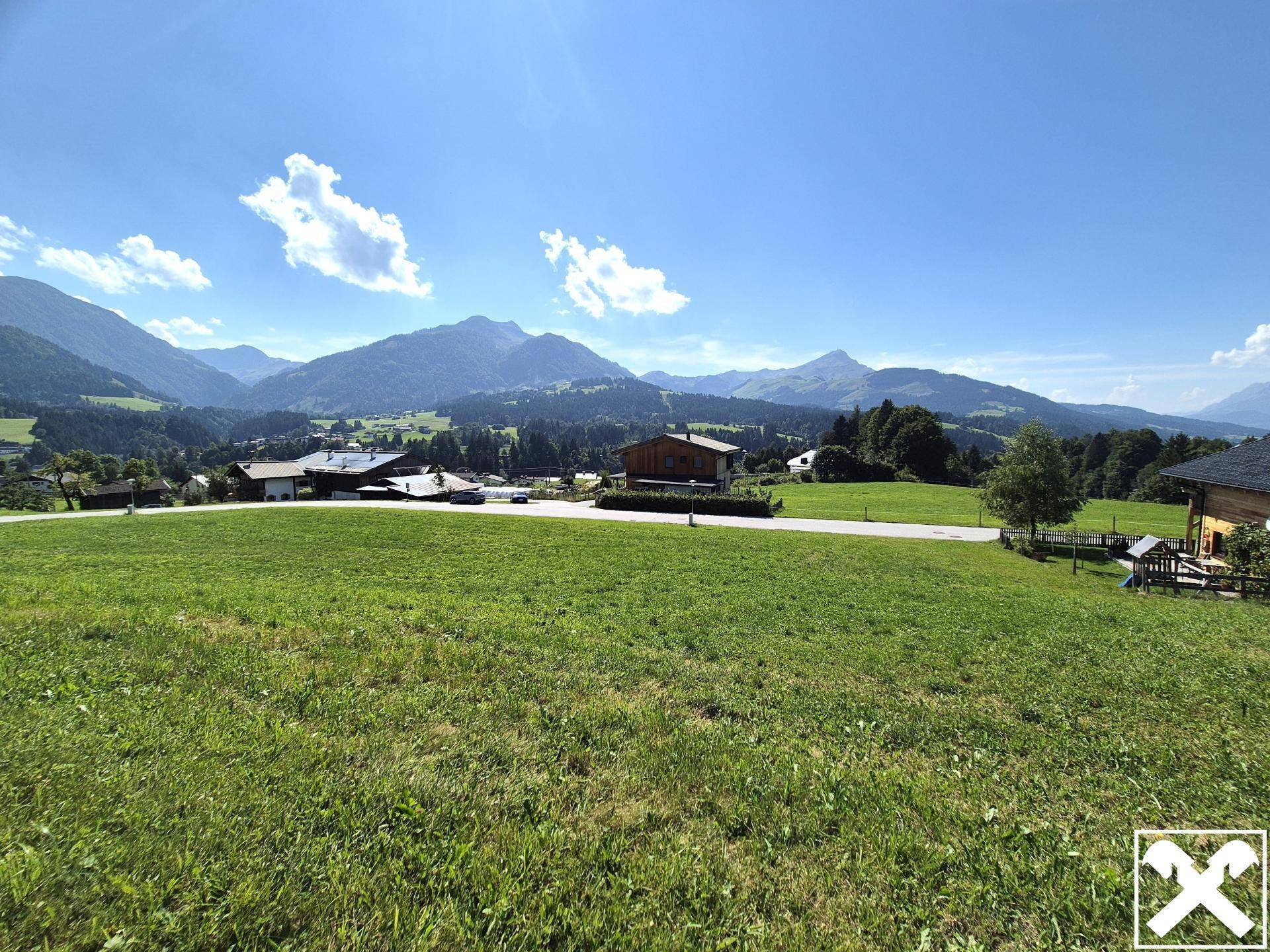 Sonnige Berglandschaft mit weiten grünen Flächen und traditionellen Häusern in der Ferne.