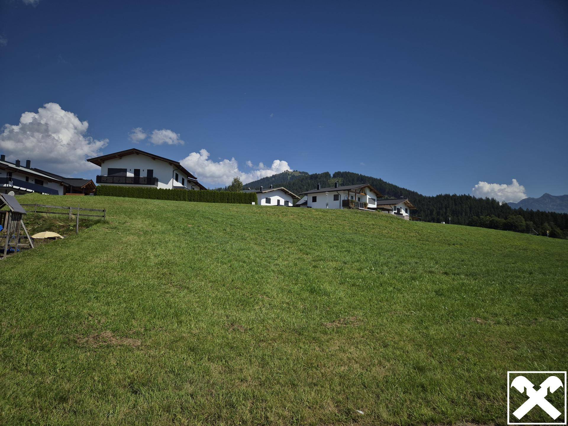Weitläufige Wiese mit Blick auf eine Reihe von Häusern am Horizont und bewölktem Himmel.