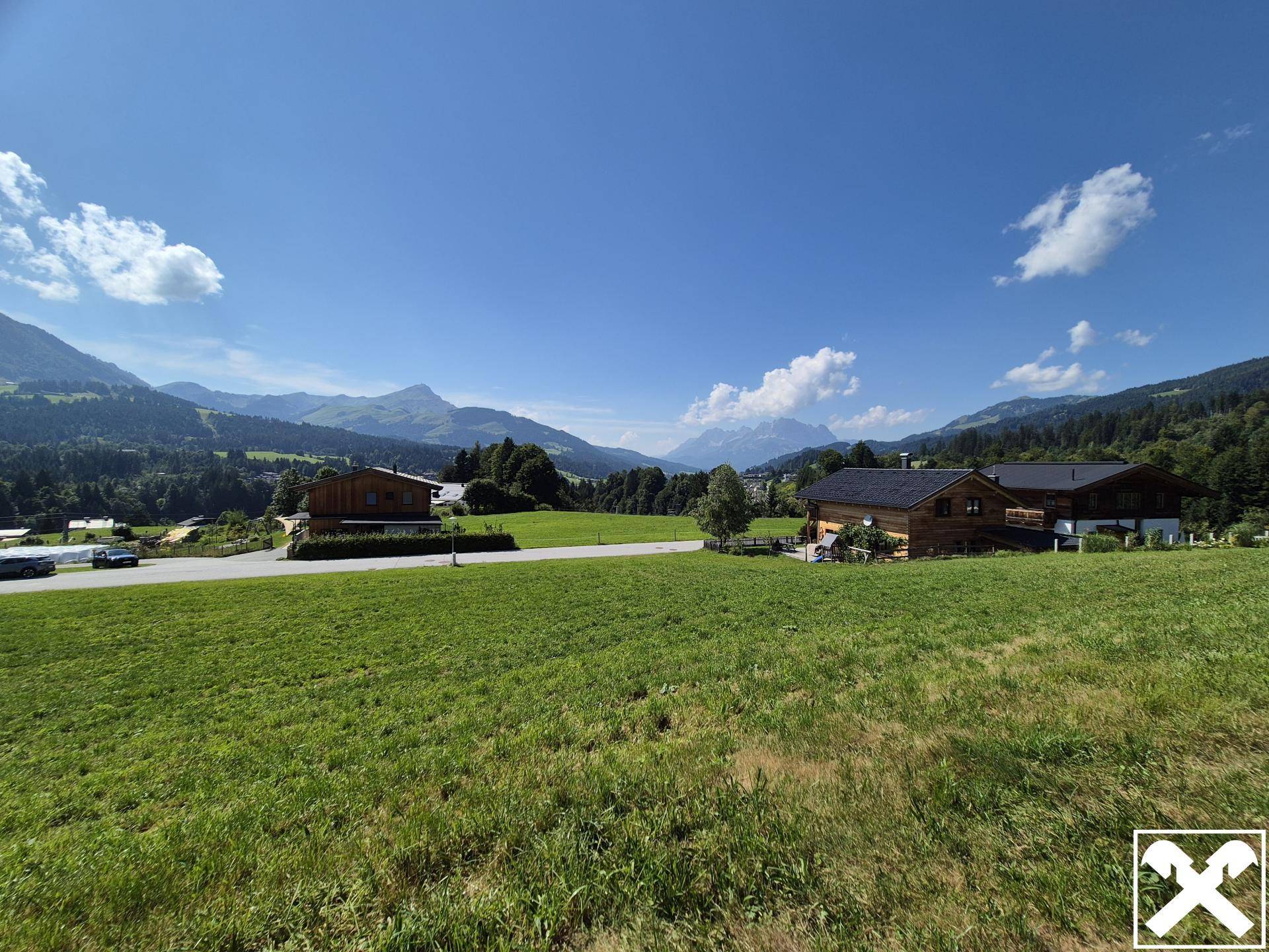 Panoramablick über grüne Wiesen und bewaldete Hügel mit majestätischen Bergen im Hintergrund.