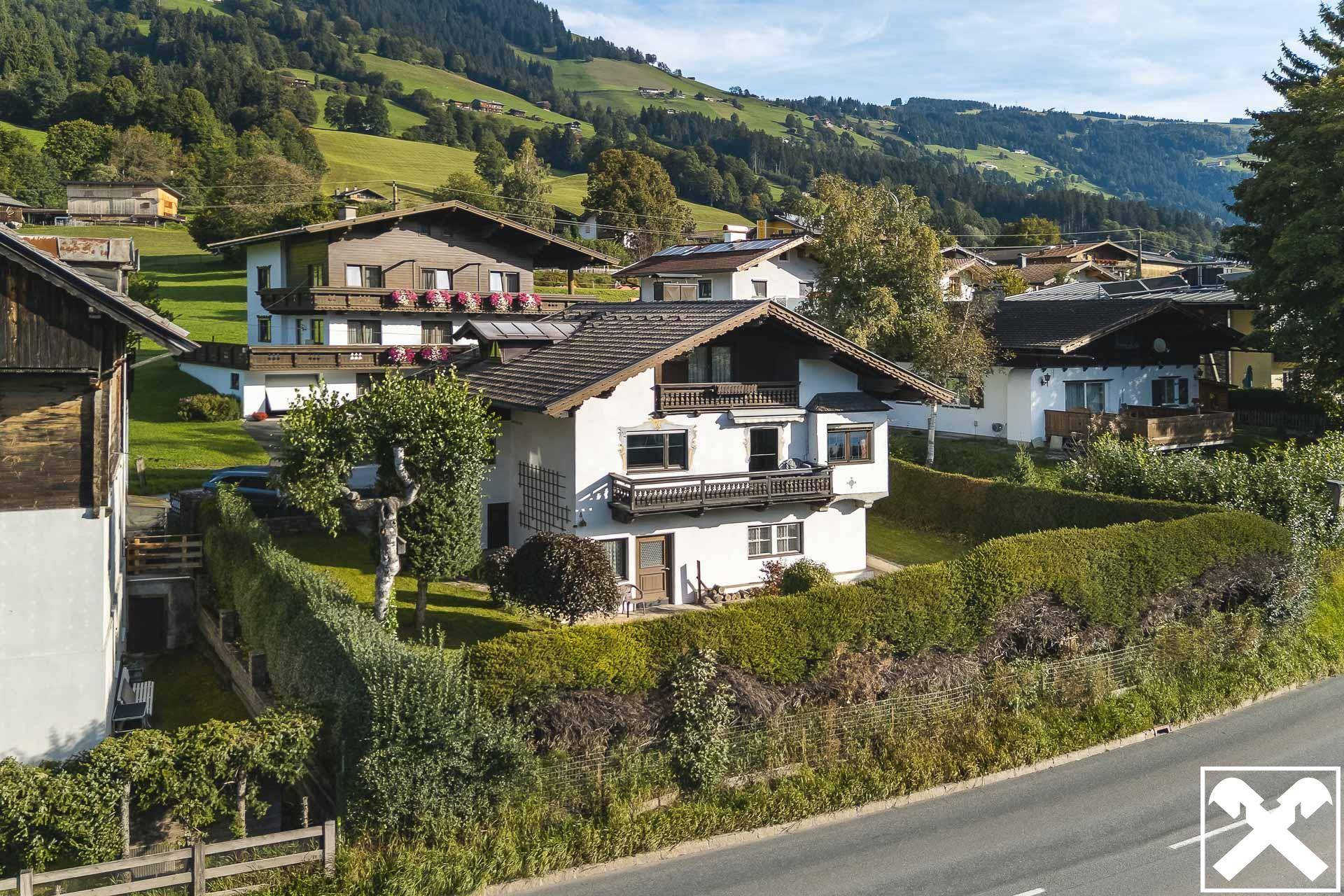 Traditionelles Haus mit Balkonen und gepflegter Hecke in bergiger Landschaft.
