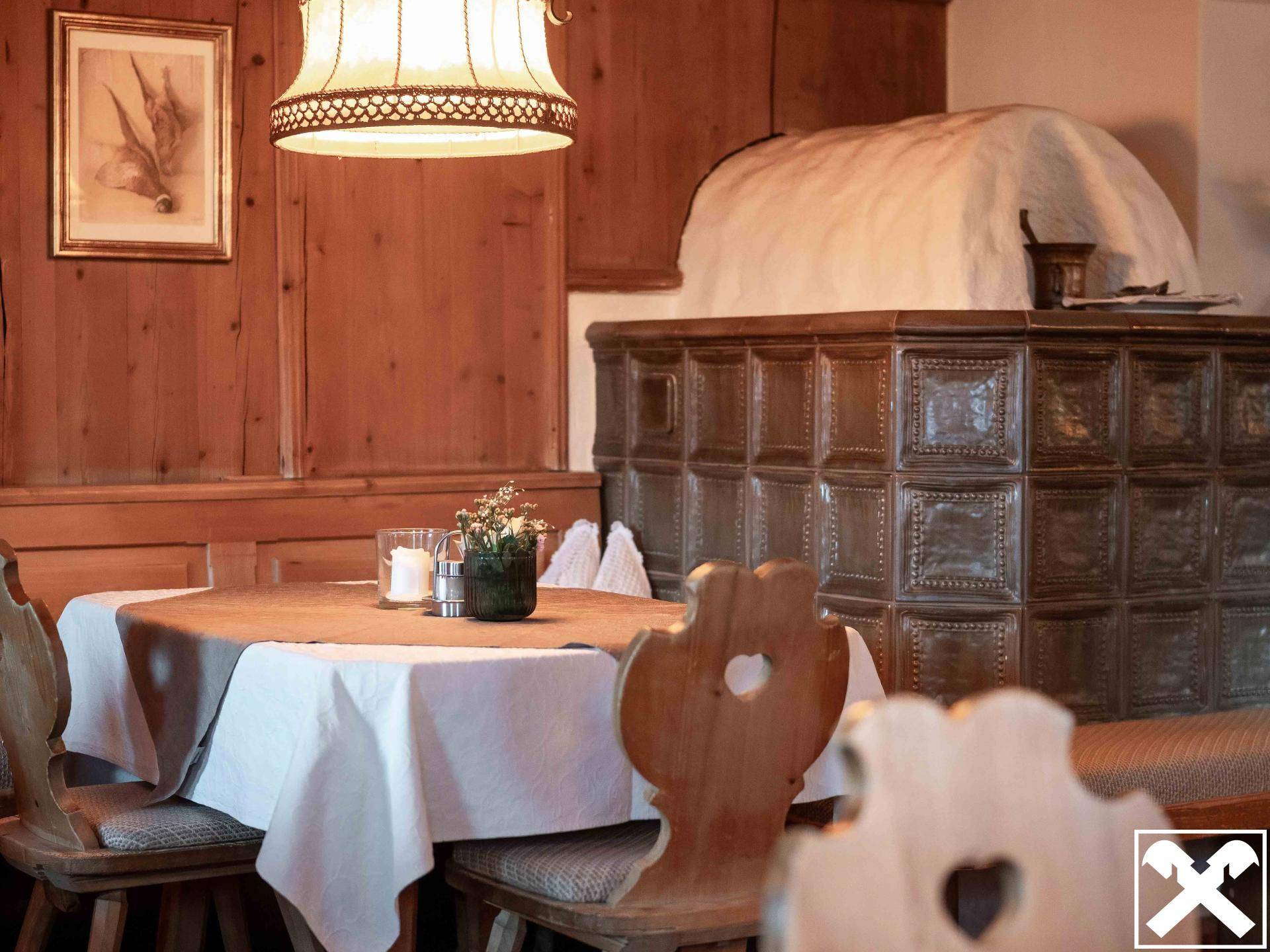 Gemütlicher Essbereich mit Holztisch, traditionellen Stühlen und einem großen, verzierten Kachelofen.