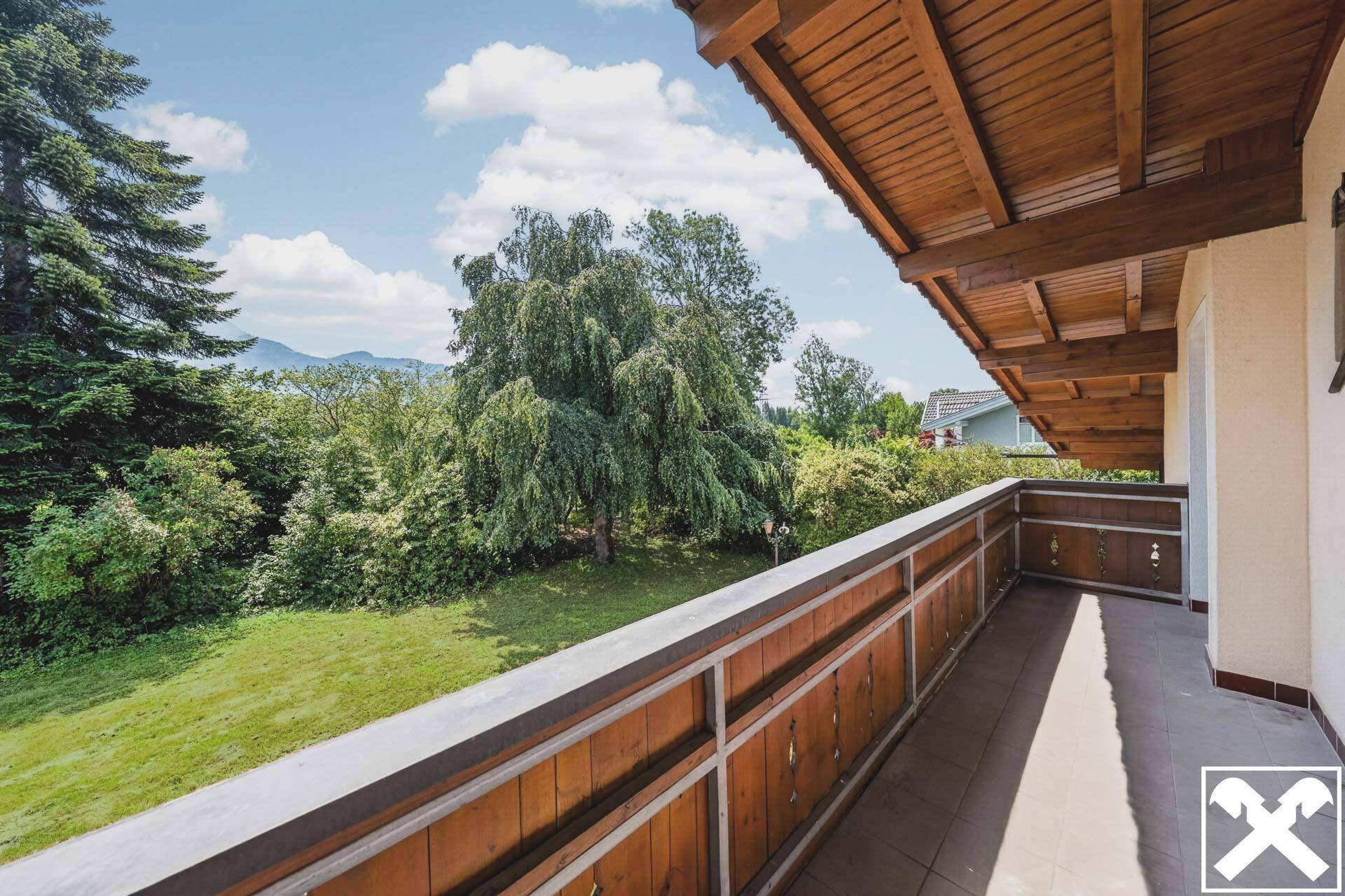Balkon mit Holzboden und Geländer, bietet einen weiten Blick ins Grüne und auf die Berge.