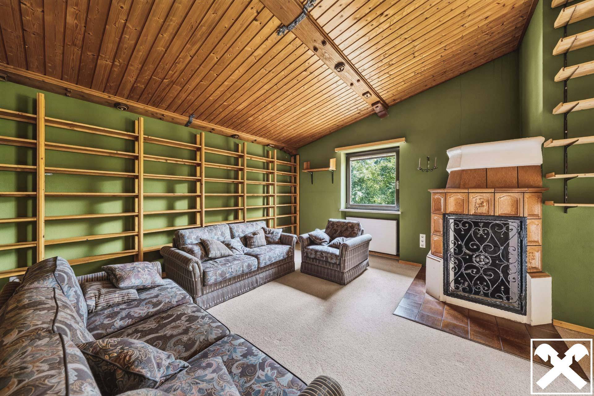 Gemütliches Wohnzimmer mit Kachelofen, grünen Wänden und rustikaler Holzbalkendecke.