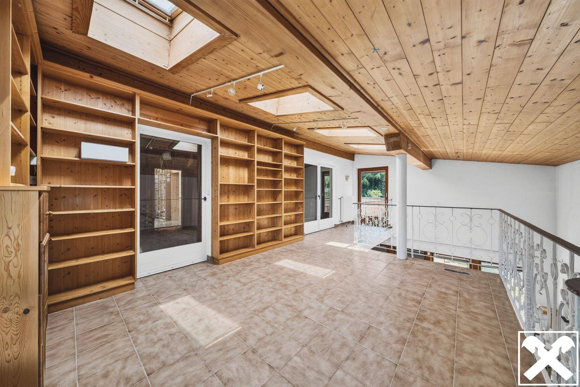 Helle Galerie mit Holzbalkendecke, Einbauregalen und Dachfenstern, die viel Licht spenden.