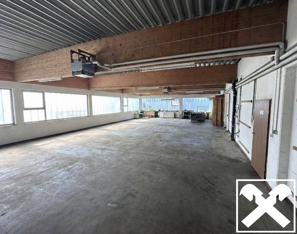 Große, leere Lagerhalle mit hohen Decken, sichtbaren Holzbalken und Betonboden, ideal für gewerbliche Nutzung.