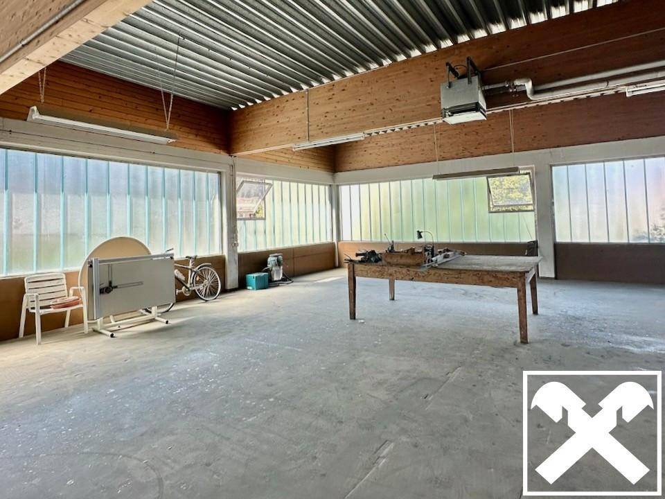 Geräumiger Werkstattbereich mit großen Fenstern, Holzverkleidung an der Decke und einigen Arbeitsgeräten.