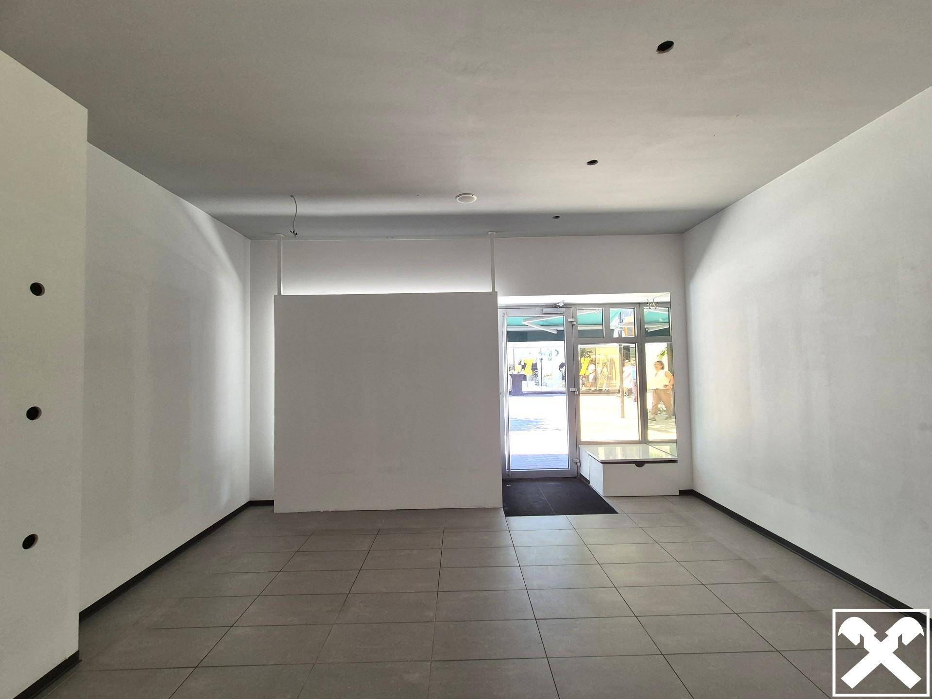 Geräumiger, leerer Geschäftsraum mit großen Fenstern zur Straße und neutralen Farben.