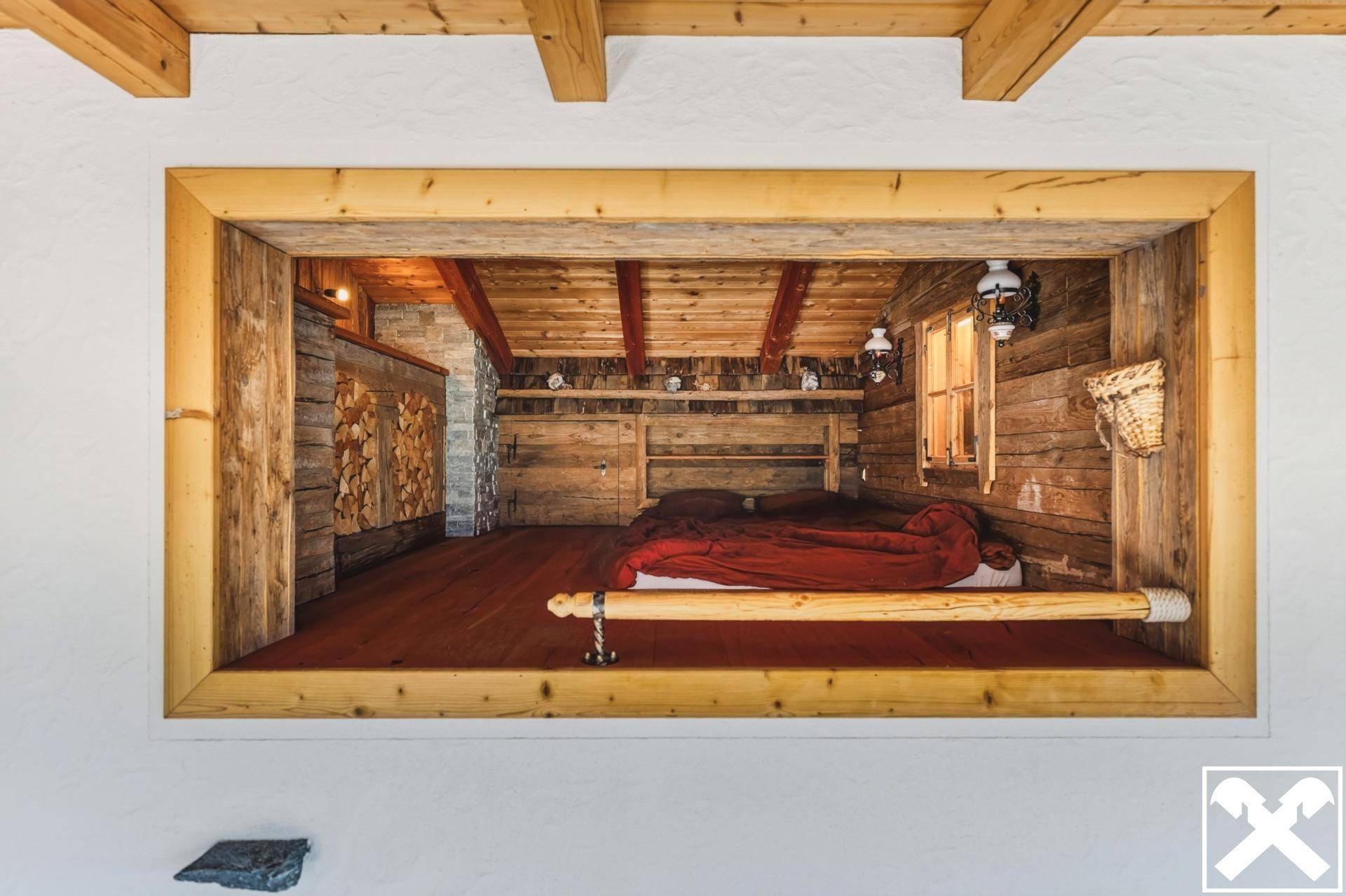 Rustikales Schlafzimmer im alpinen Stil mit Holzwänden, Holzbalken und einem erhöhten Bett.