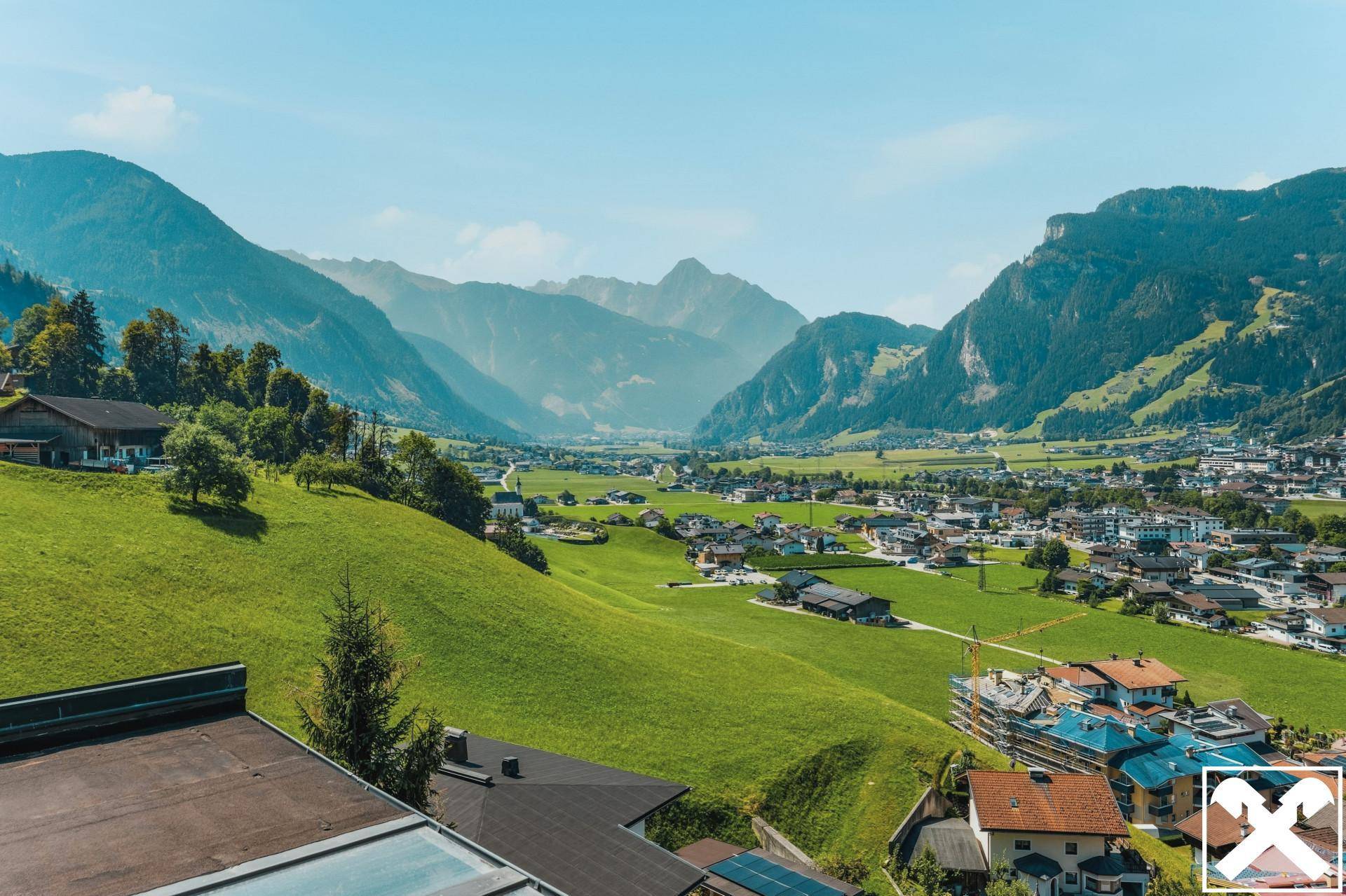 Panoramablick auf ein malerisches Tal mit einem Dorf, umgeben von majestätischen Bergen und grünen Hügeln.