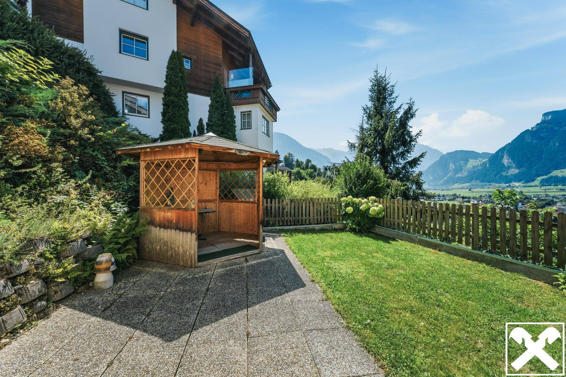 Ruhiger Gartenbereich mit Rasen, Holzpavillon und Blick auf die umliegende Berglandschaft.