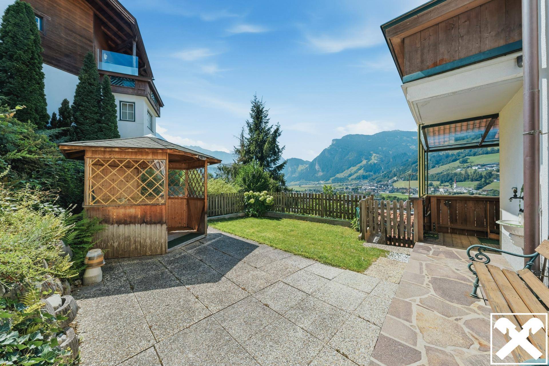 Gepflegter Gartenbereich mit Rasenfläche, gepflasterter Terrasse und einem Holzpavillon mit Bergblick.