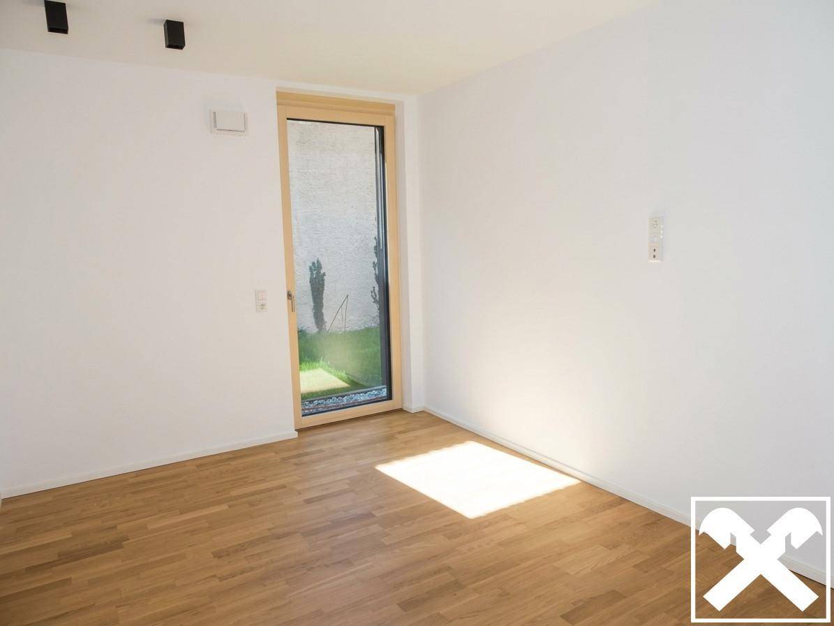 Helles Zimmer mit Parkettboden und bodentiefem Fenster, das viel Tageslicht hereinlässt.