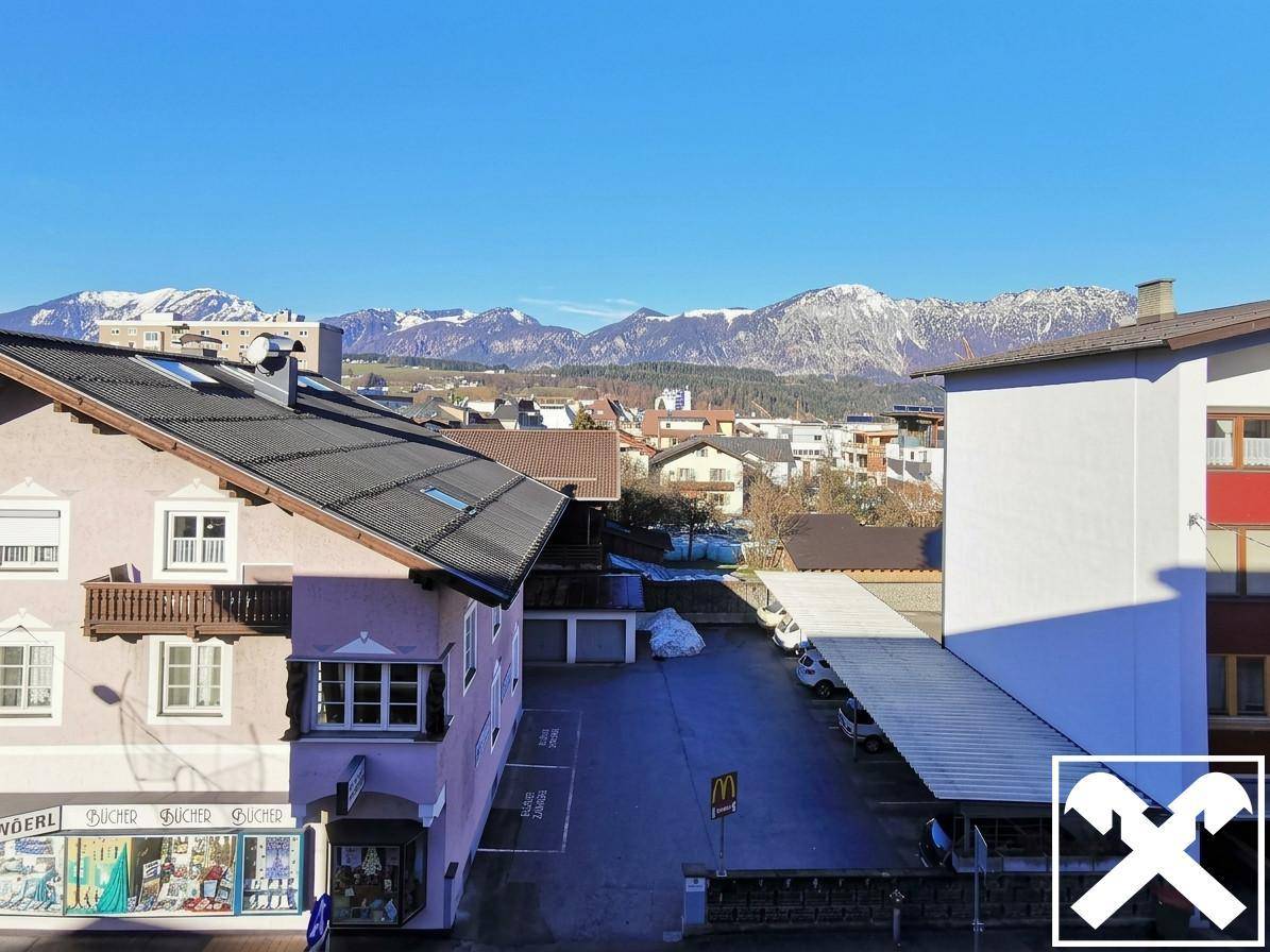 Panoramablick auf die umliegende Stadtlandschaft mit majestätischen Bergen im Hintergrund unter blauem Himmel.