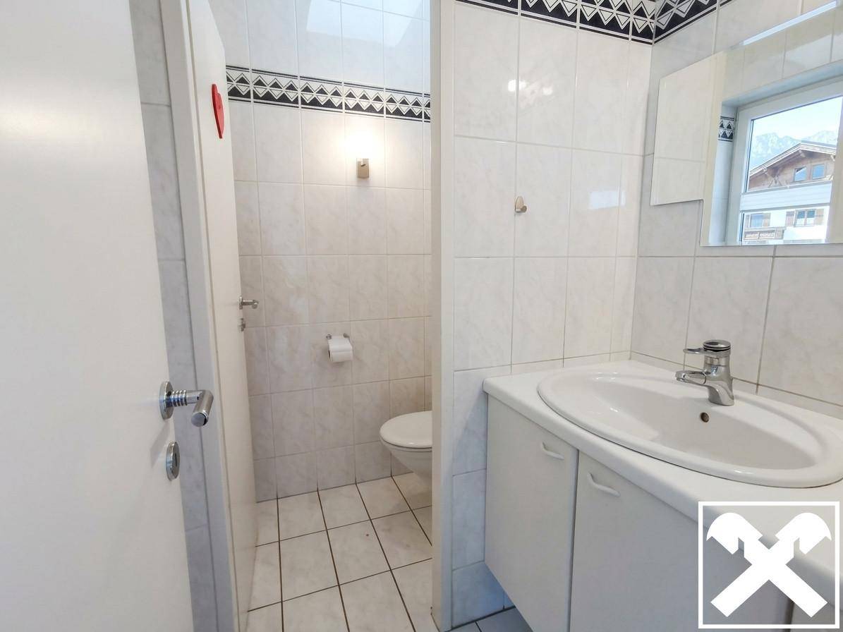 Helles Badezimmer mit weißen Fliesen, Waschbecken mit Unterschrank und separatem WC-Bereich.