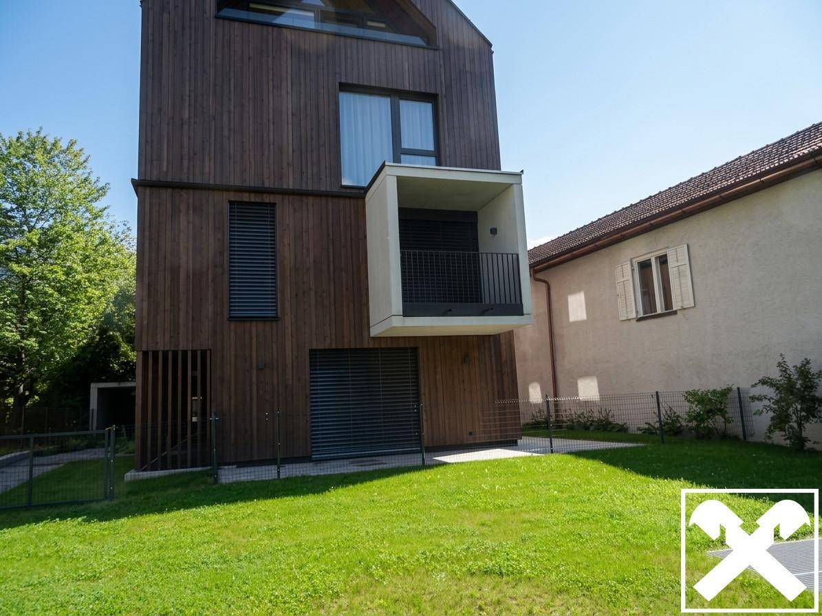 Moderne Holzfassade eines Neubaus mit Balkon und großen Fenstern in sonniger Umgebung.