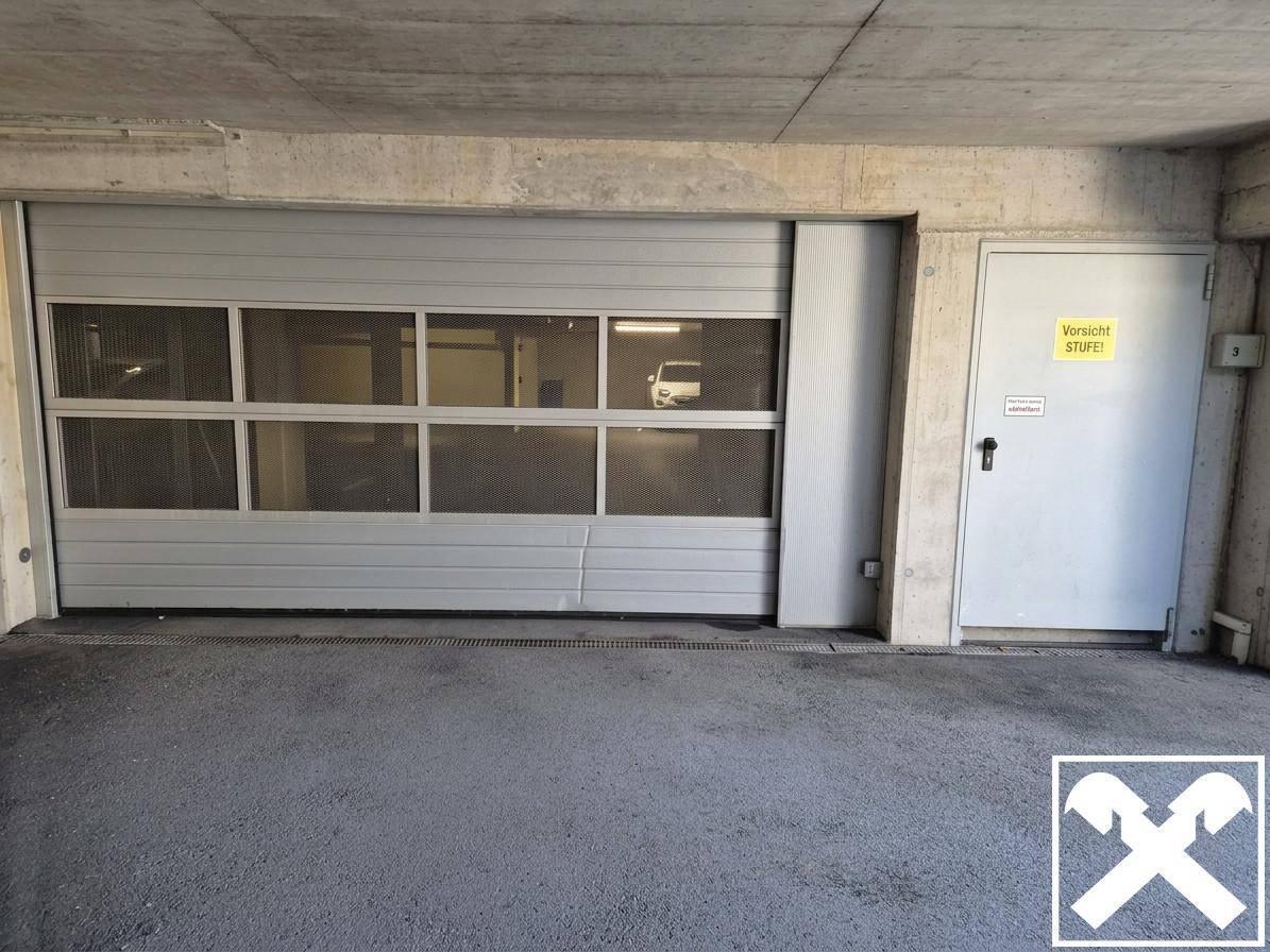Garagentor mit Fenstern und separater Zugangstür in einer Tiefgarage mit Betonwänden und -decke.