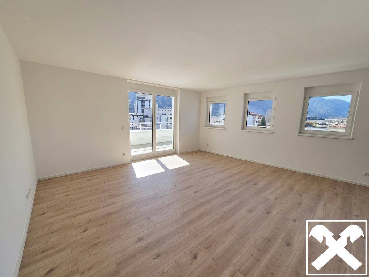 Helles, leeres Wohnzimmer mit Laminatboden und Zugang zu einem Balkon mit Bergblick.