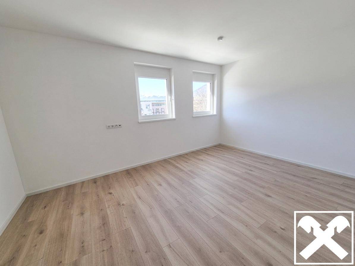 Leeres Schlafzimmer mit hellem Laminatboden und zwei Fenstern, bereit zur individuellen Gestaltung.