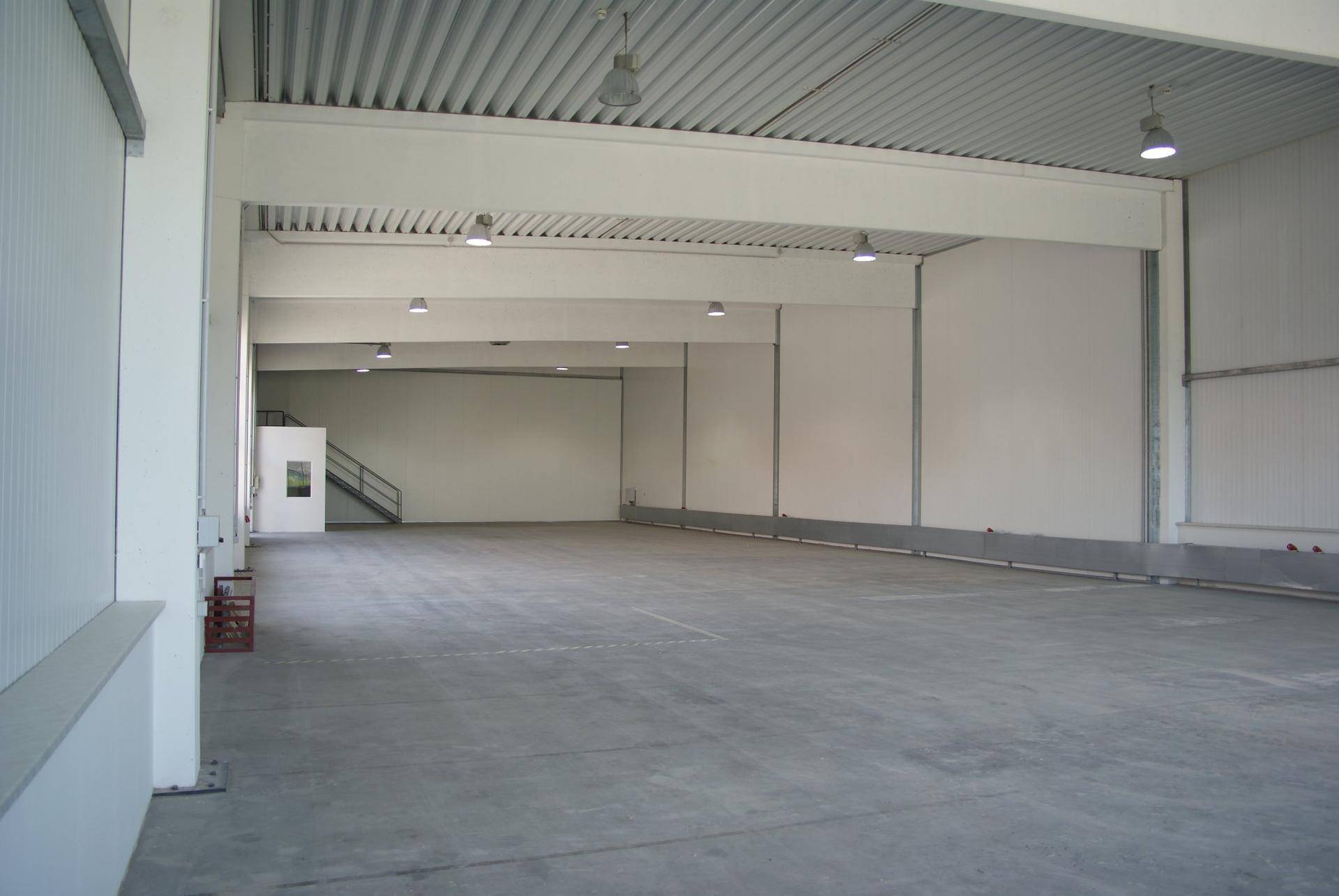 Tiefer Blick in die leere Lagerhalle mit hohen Decken, Betonboden und einer klaren, funktionalen Gestaltung.