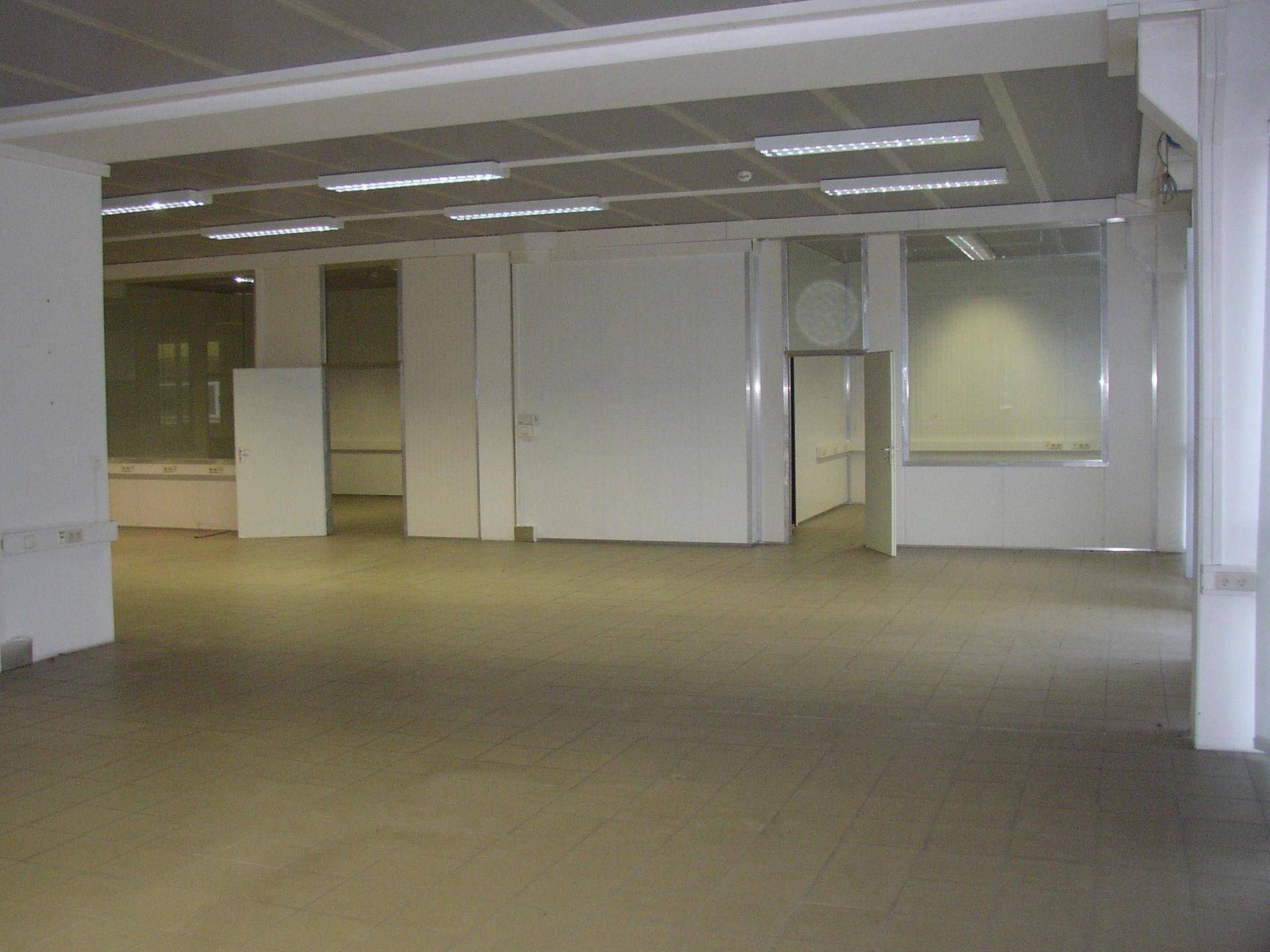 Weitläufiger Gewerberaum mit hellen Fliesen und modularen Trennwänden, ideal für Büros.
