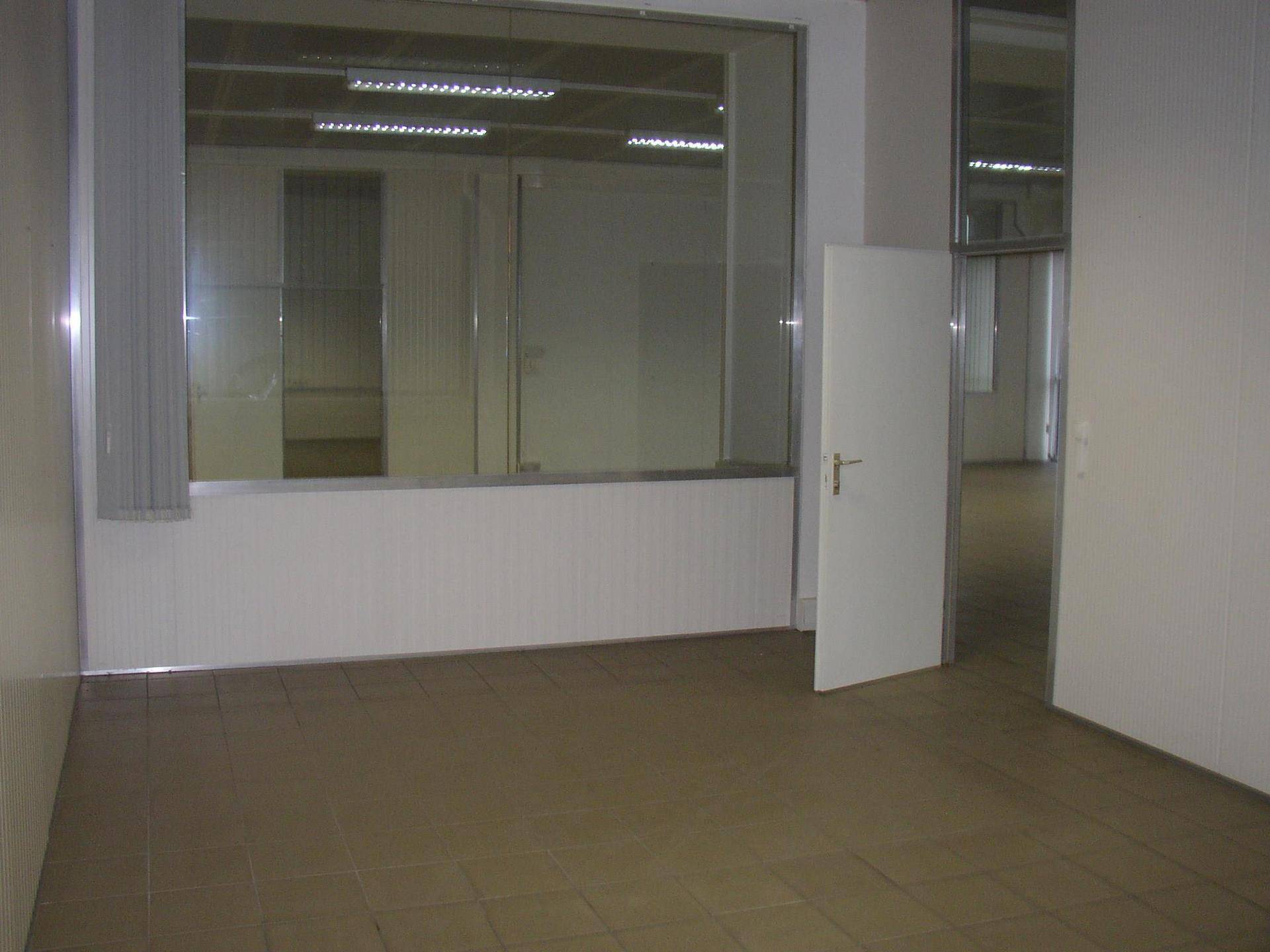 Kleinerer Bereich eines Gewerberaums mit Fliesenboden und Fenster mit Jalousien.