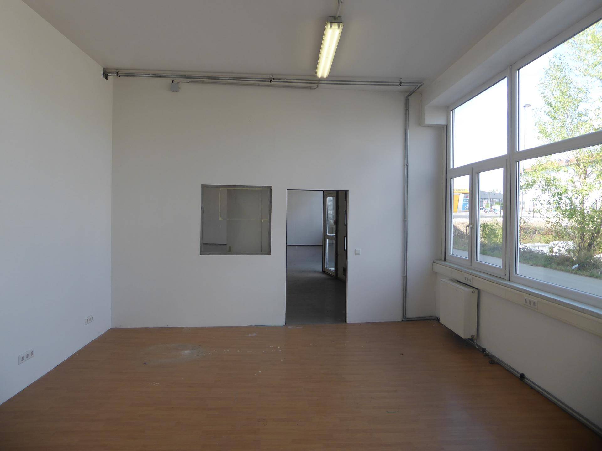Helles Büro mit Laminatboden, großen Fenstern und einem Heizkörper unter dem Fenster.