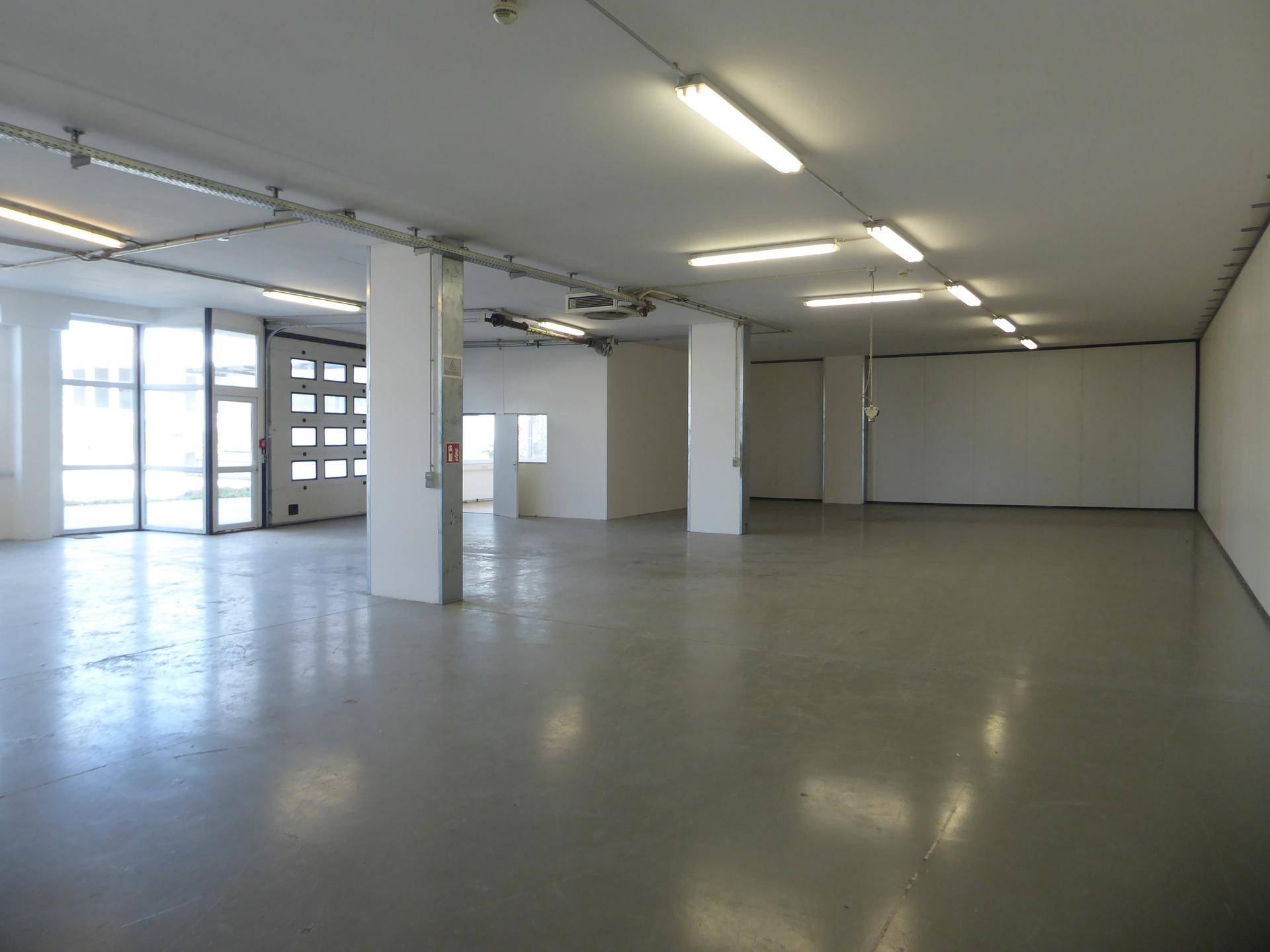 Großer, leerer Lagerraum mit Betonboden, Säulen und Leuchtstoffröhren an der Decke.