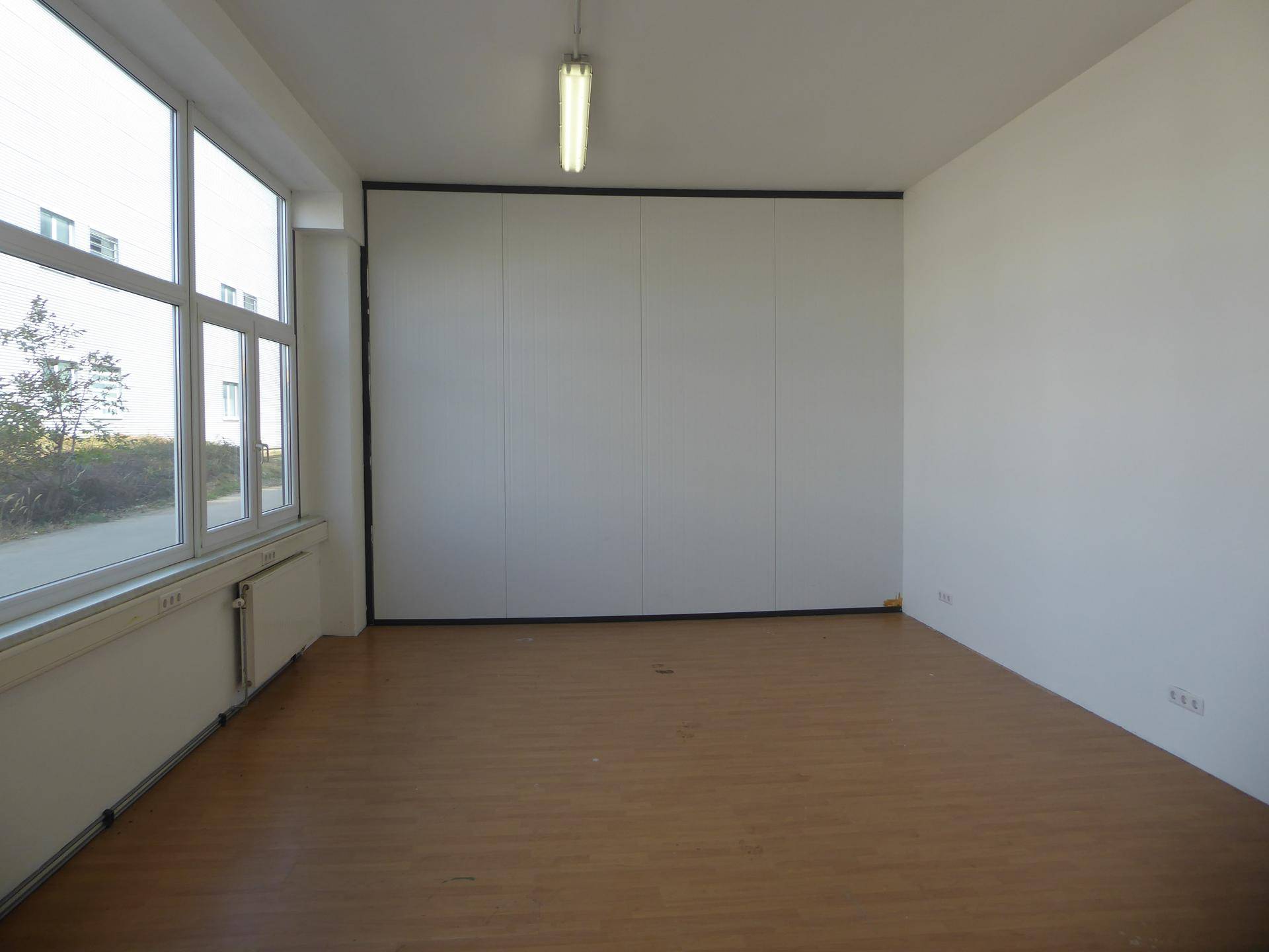 Leeres Büro mit Laminatboden, großen Fenstern und einer weißen Trennwand.