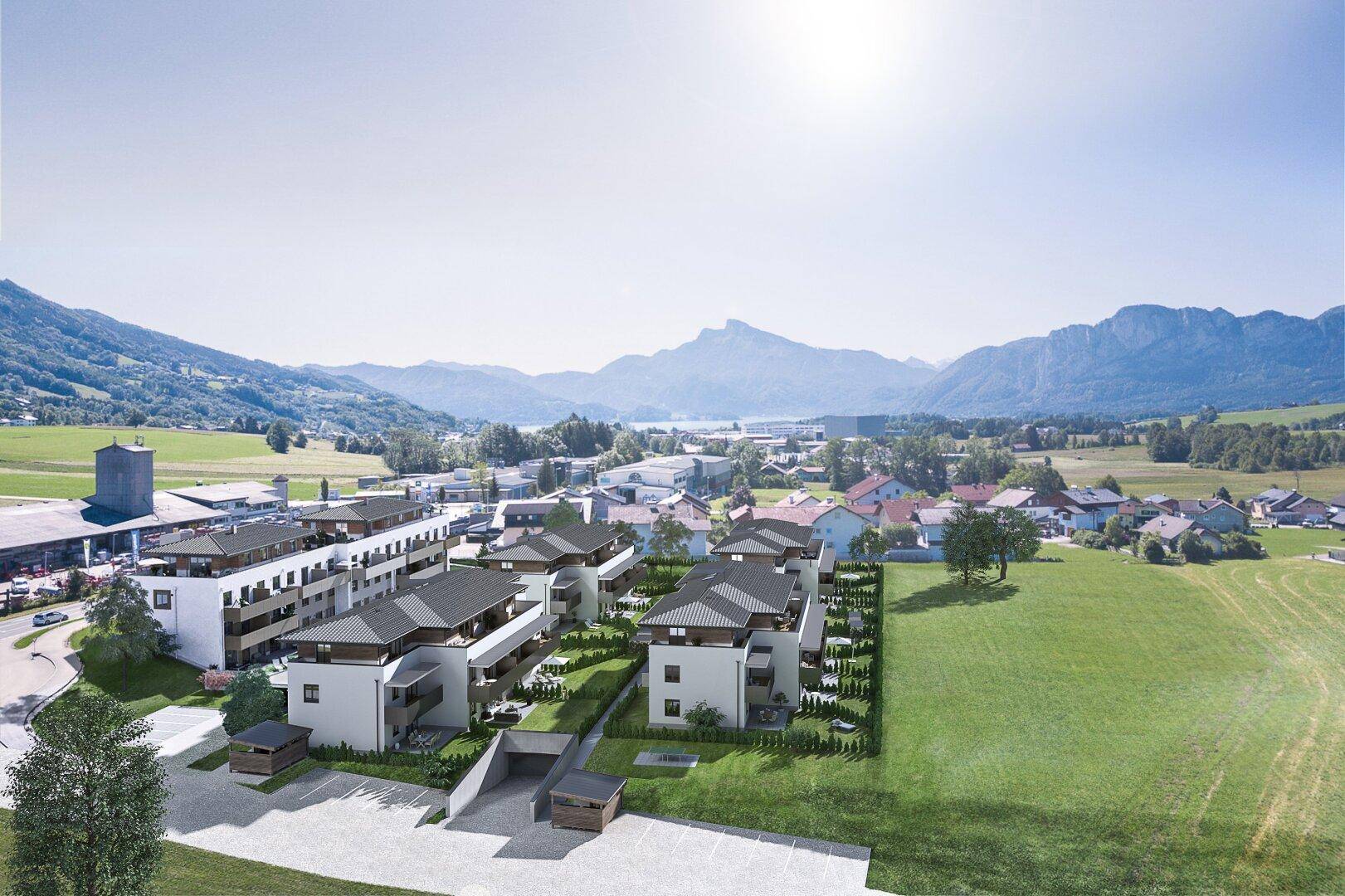 Luftaufnahme eines modernen Wohnkomplexes in einer malerischen Berglandschaft mit See im Hintergrund.