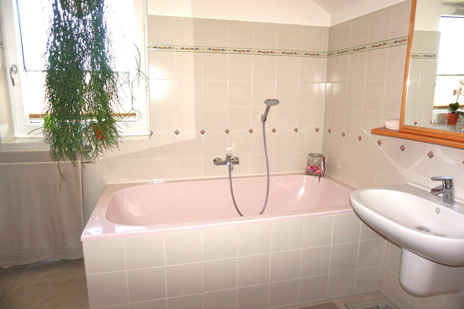 Badezimmer im 80er-Jahre-Stil mit rosa Badewanne, Fliesen und Fenster.