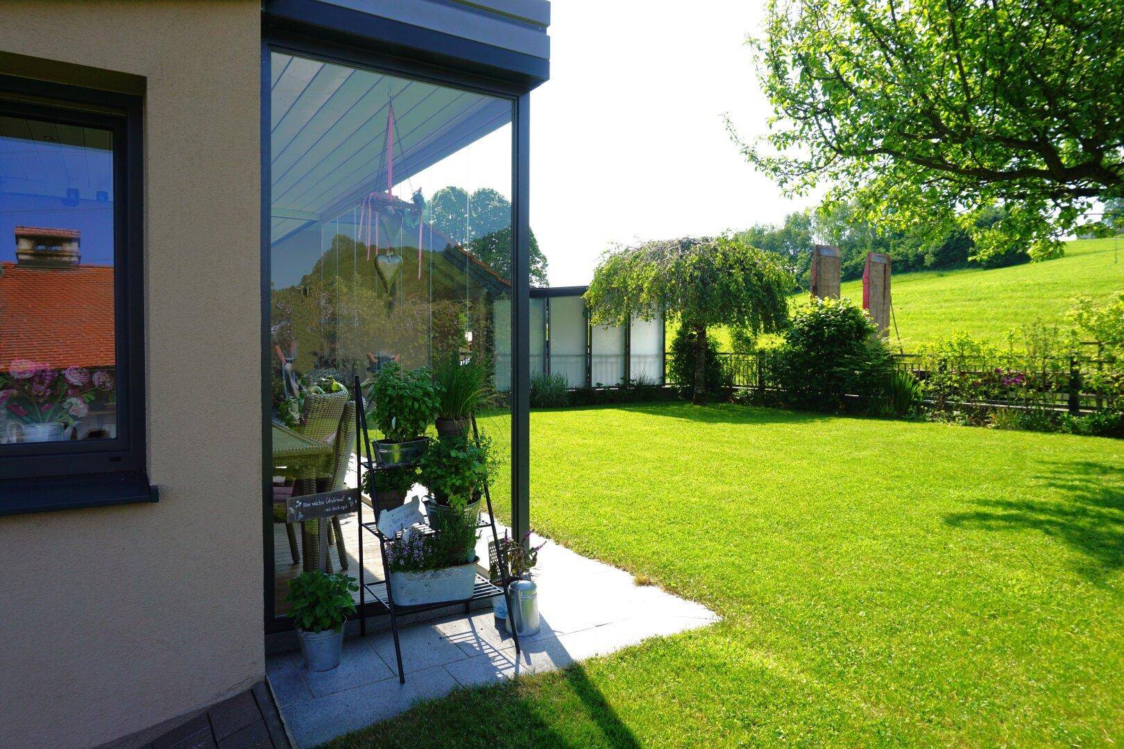 Grüne Rasenfläche neben einem Wintergarten mit weitem Blick auf die Landschaft.