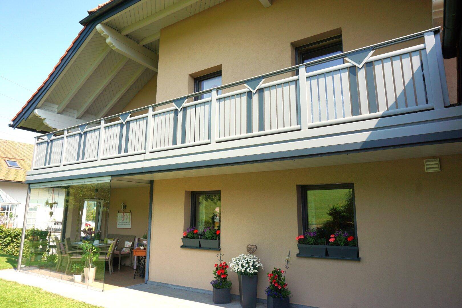 Detailansicht der Hausfassade mit Balkon, Blumenkästen und verglastem Wintergarten im Erdgeschoss.
