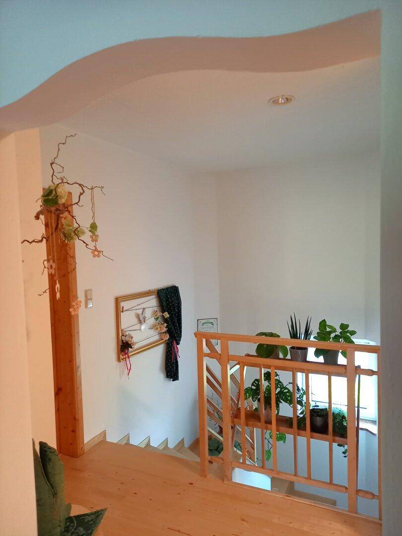 Heller Treppenaufgang mit Holzgeländer und dekorativen Pflanzen, gut beleuchtet.