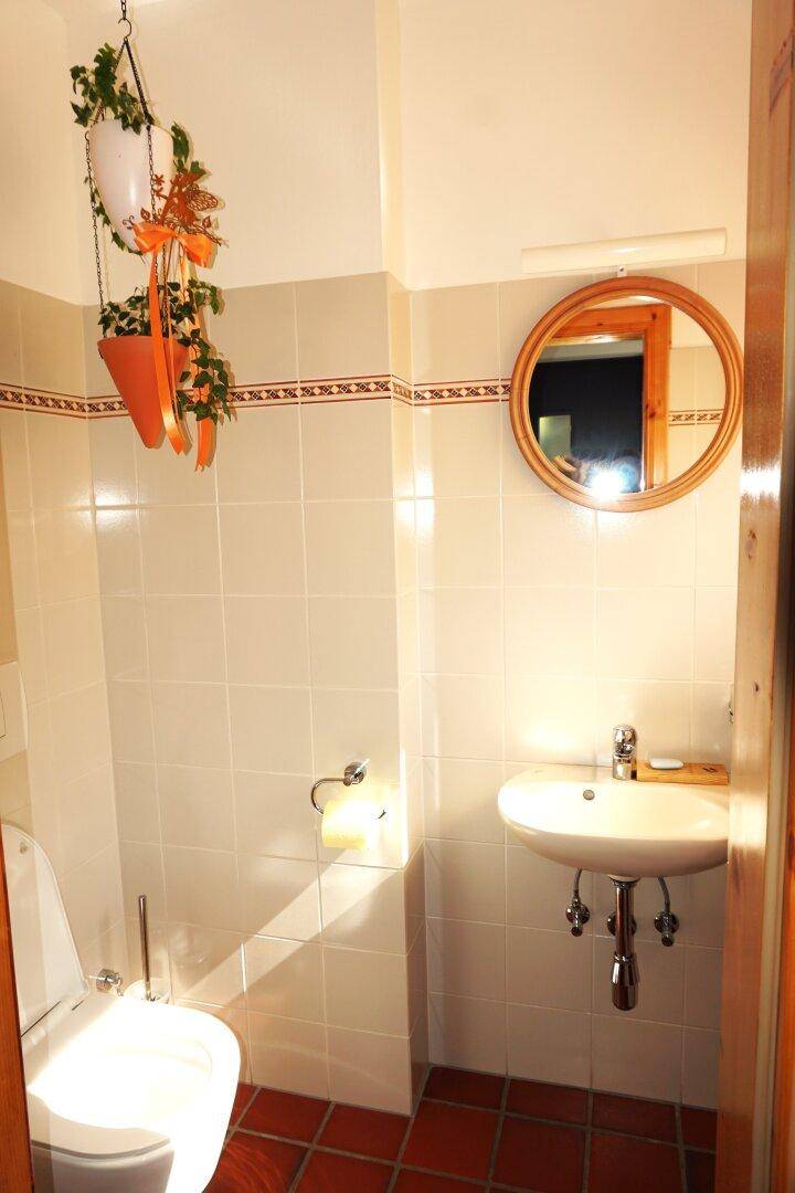 Separate Gästetoilette mit Waschbecken, Spiegel und Terrakottafliesen.