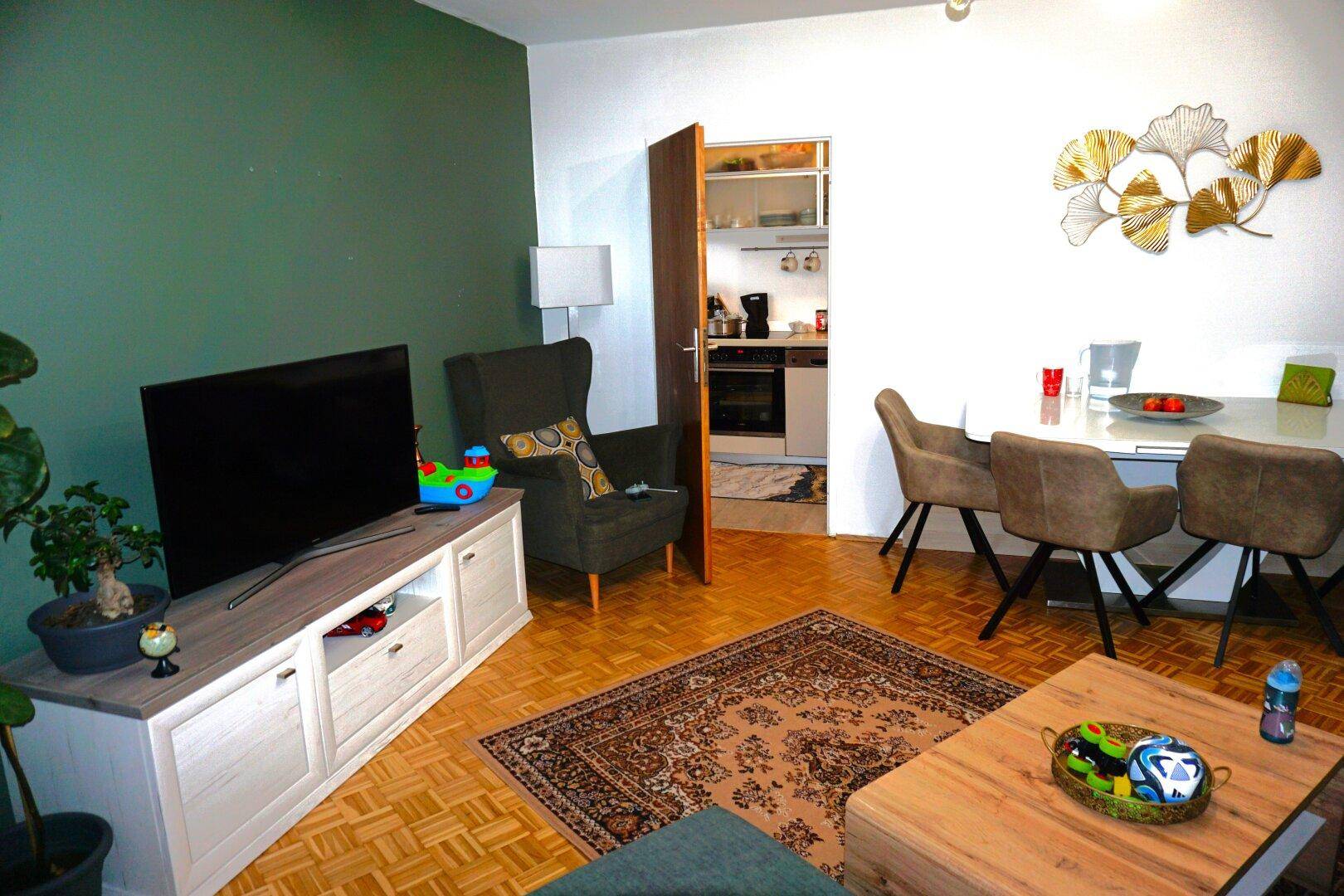 Offener Wohn- und Essbereich mit Fernseher, Esstisch und direktem Zugang zur Küche.