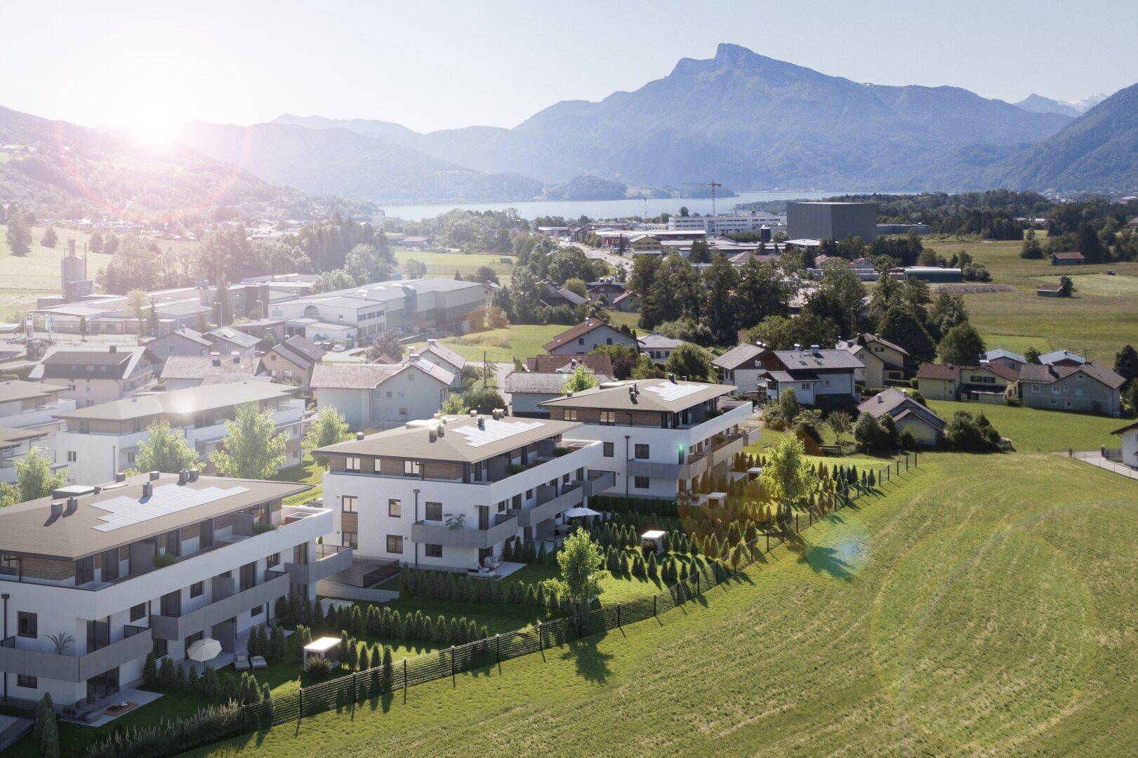 Moderne Wohngebäude in sonniger Lage mit Blick auf Berge und See, umgeben von grünen Feldern.