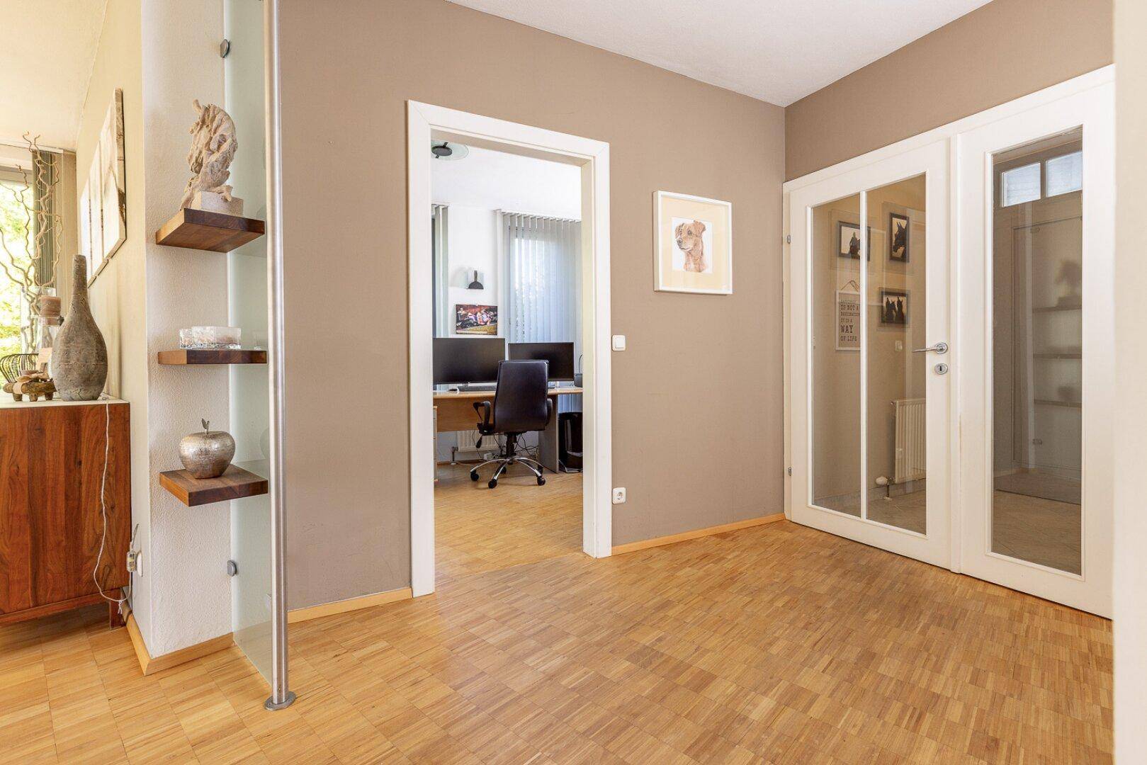 Heller Flur mit Parkettboden und Zugang zu einem Arbeitszimmer durch eine Glastür.