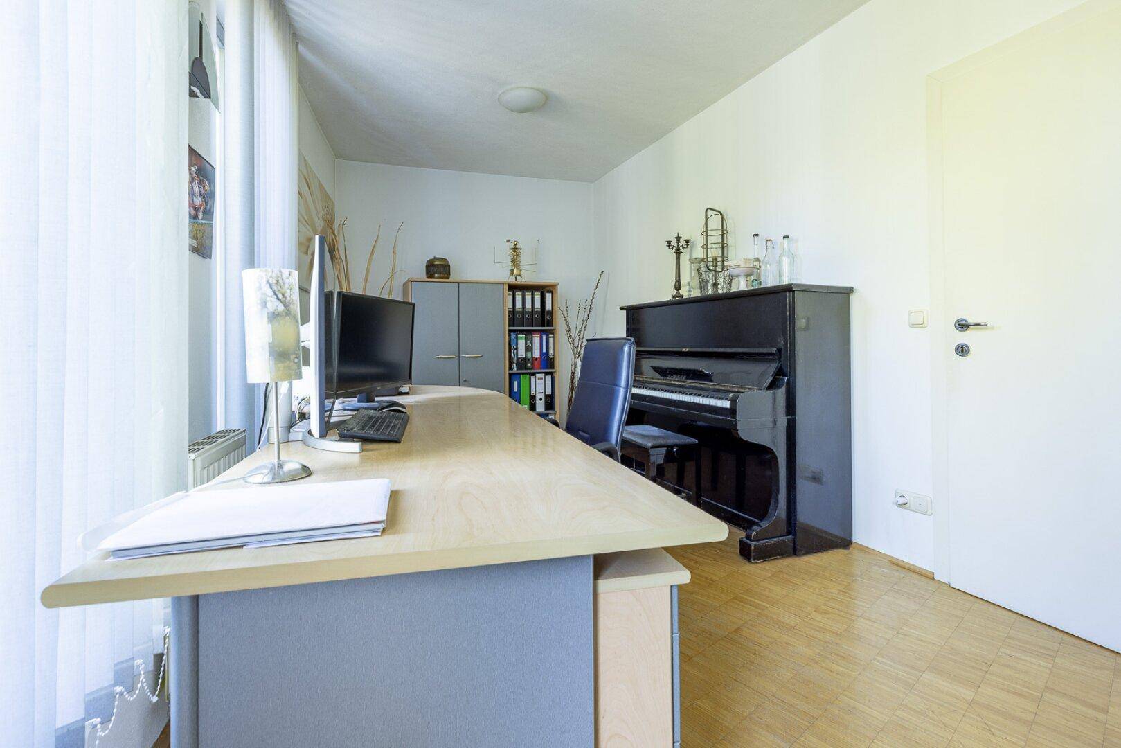 Ruhiges Arbeitszimmer mit Schreibtisch, Klavier und Fenster für natürliches Licht.