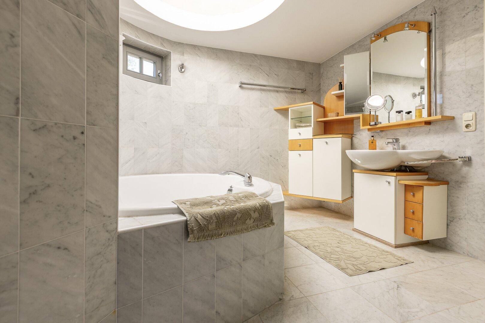 Elegantes Badezimmer mit Marmorfliesen, Waschtisch und runder Deckenbeleuchtung.