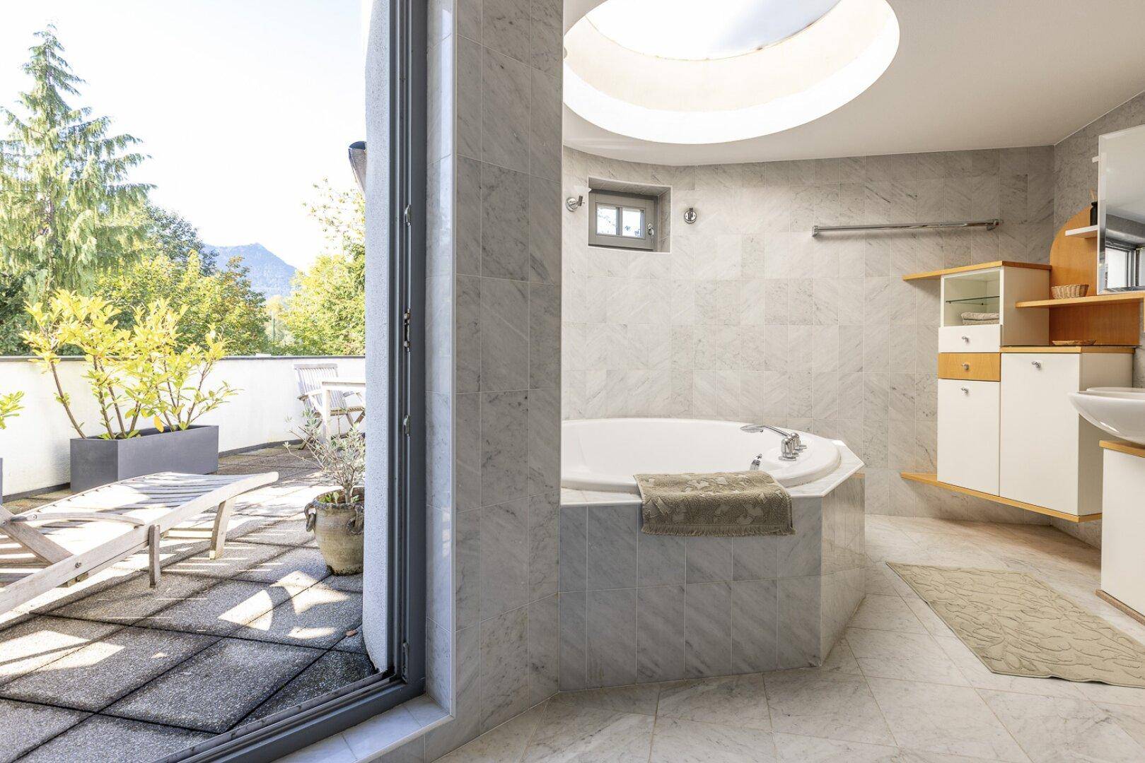 Helles Badezimmer mit Marmorfliesen, Badewanne und direktem Zugang zur Terrasse.